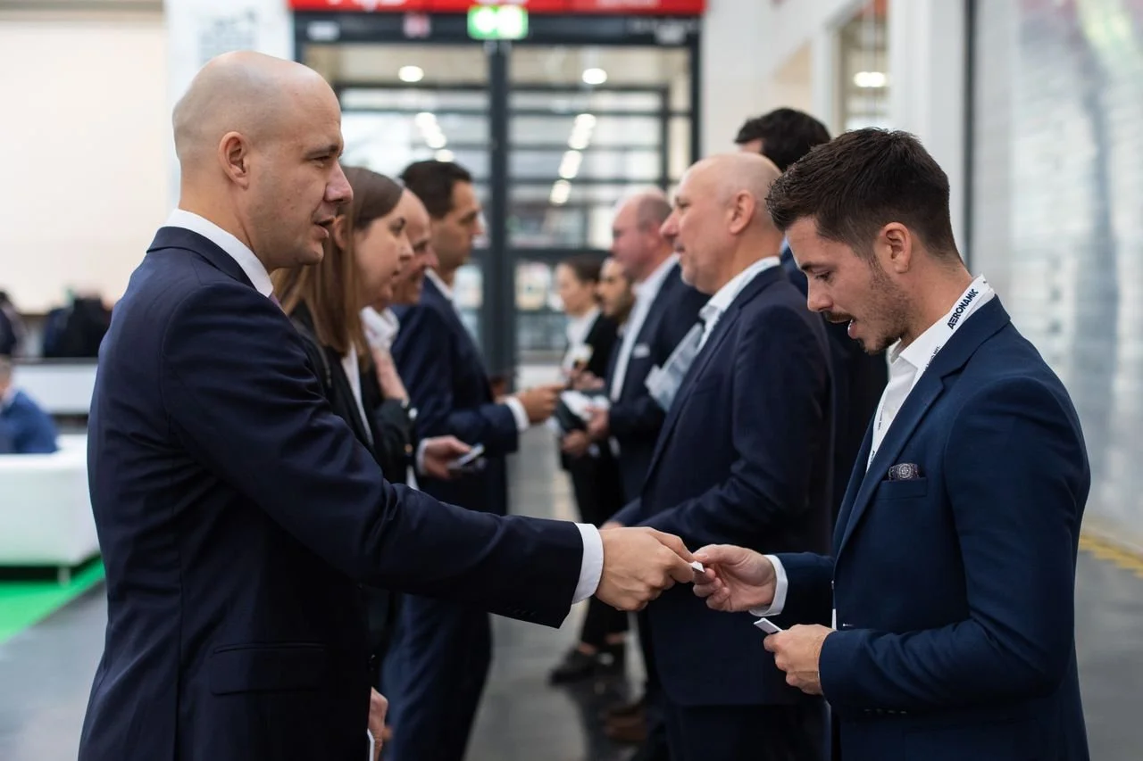 A group of business professionals dressed in suits standing in a line at an event, exchanging business cards.