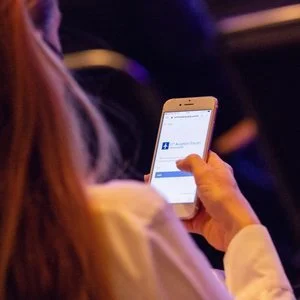 A person holding a smartphone in their hand, scrolling or interacting with the device, in a dark environment.