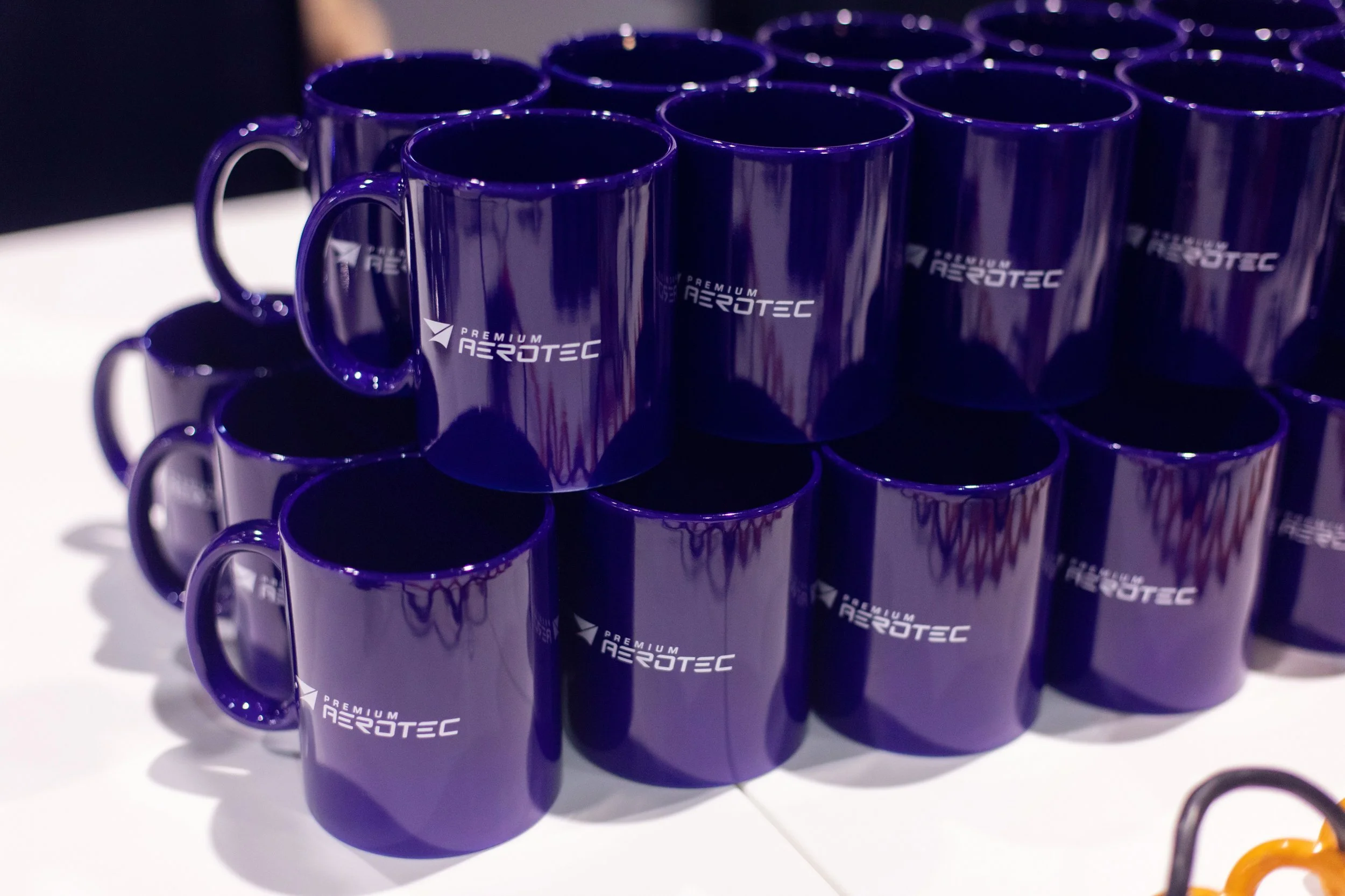 Multiple purple ceramic mugs with 'Premium AeroTec' logo on white surface, arranged in a pyramid shape.