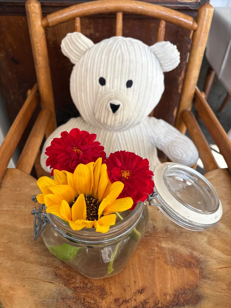 Teddy auf einem alten Kinderstuhl mit Sonnenblume und Dahlien