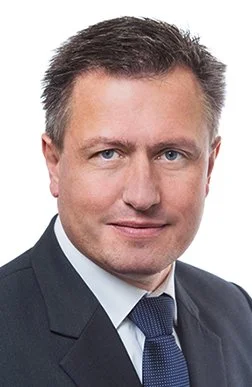 Porträt eines Mannes in formeller Kleidung vor weißem Hintergrund.