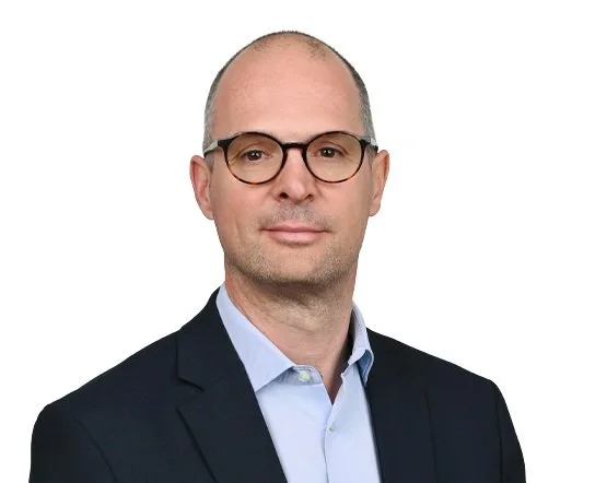 Porträt eines Mannes mit Brille in Geschäftskleidung vor weißem Hintergrund.