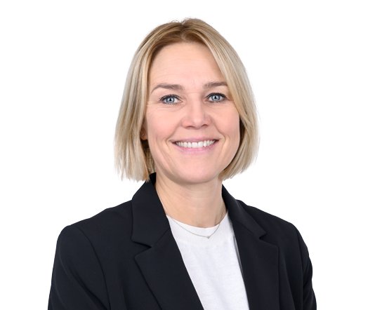 Eine blonde Frau trägt einen schwarzen Blazer und ein weißes Hemd, lächelt vor weißem Hintergrund.