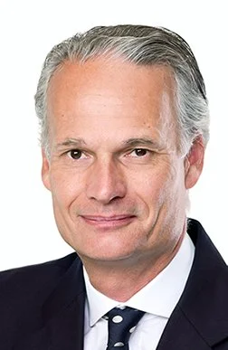 Nahaufnahme eines älteren Mannes in formeller Kleidung, graues Haar, mit einem leichten Lächeln
