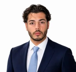 Porträt eines jungen Mannes in formeller dunkler Anzugjacke, weißem Hemd und hellblauer Krawatte auf weißem Hintergrund.
