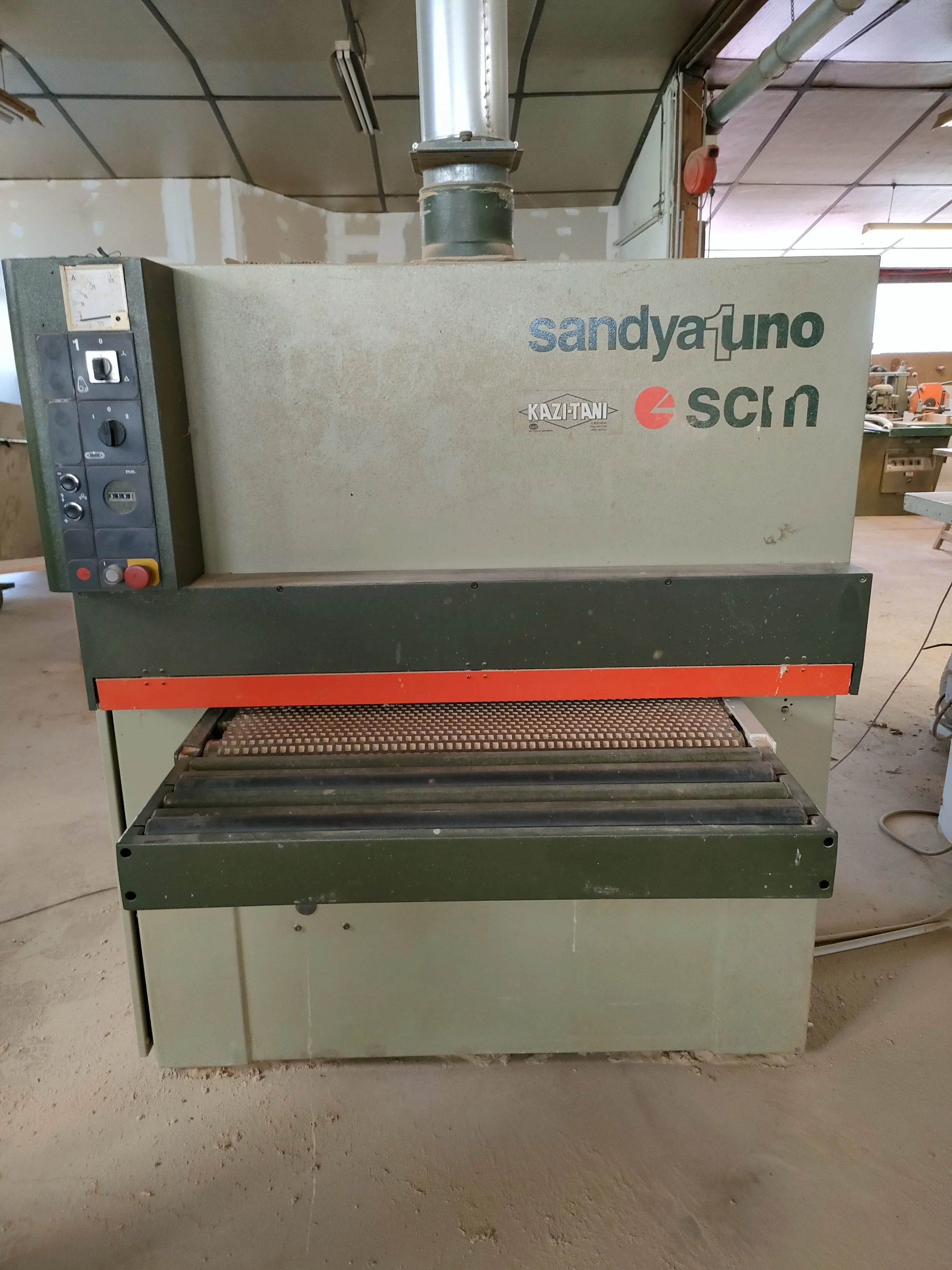 Machine de sciage industrielle dans un atelier de fabrication, marque Sandyuno et autres logos, sur un sol en ciment