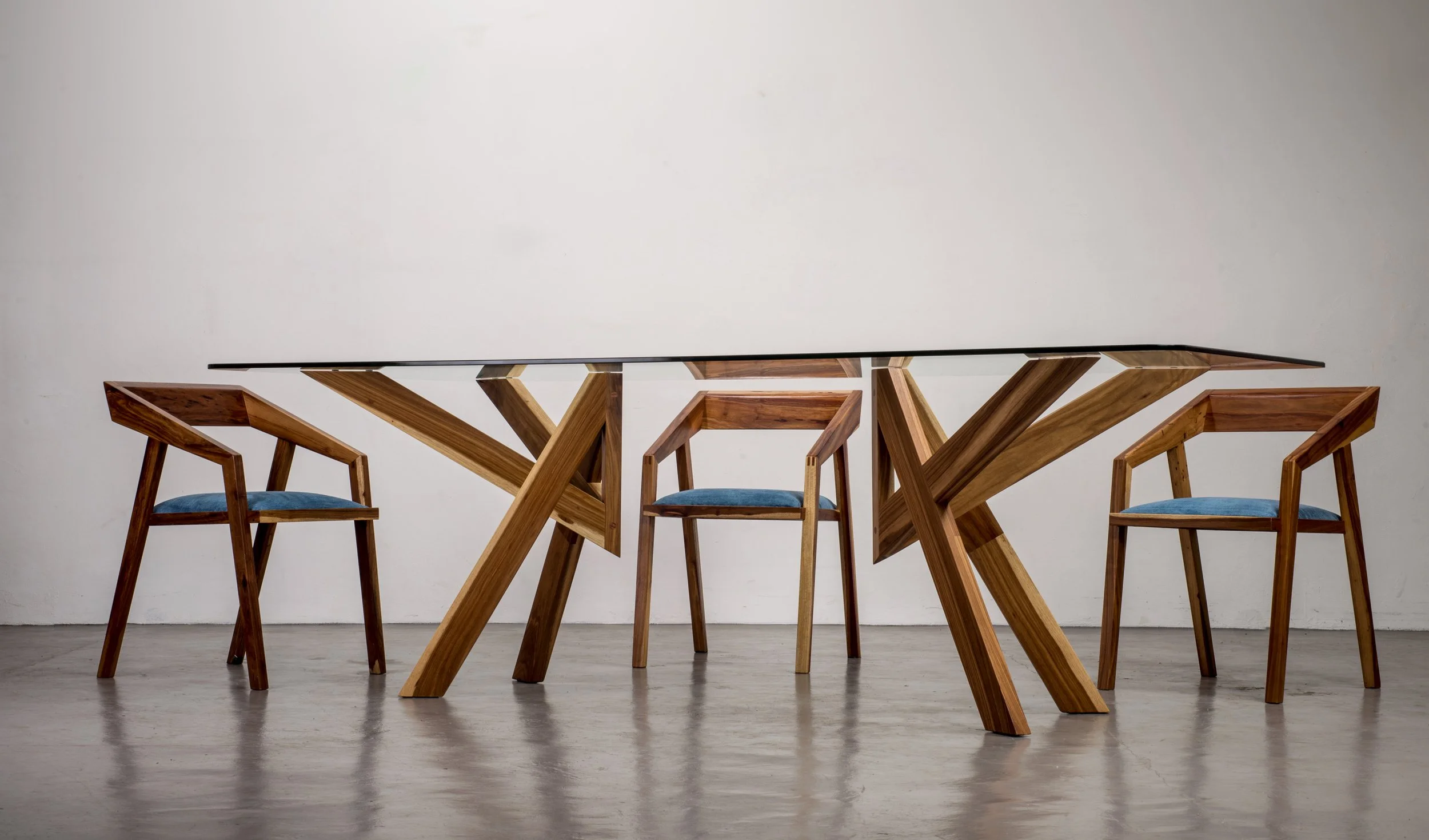 Table à manger sur mesure en bois au design moderne et unique, avec plateau en verre et chaises contemporaines aux assises en tissu bleu. Une création alliant matériaux nobles, fonctionnalité et élégance.