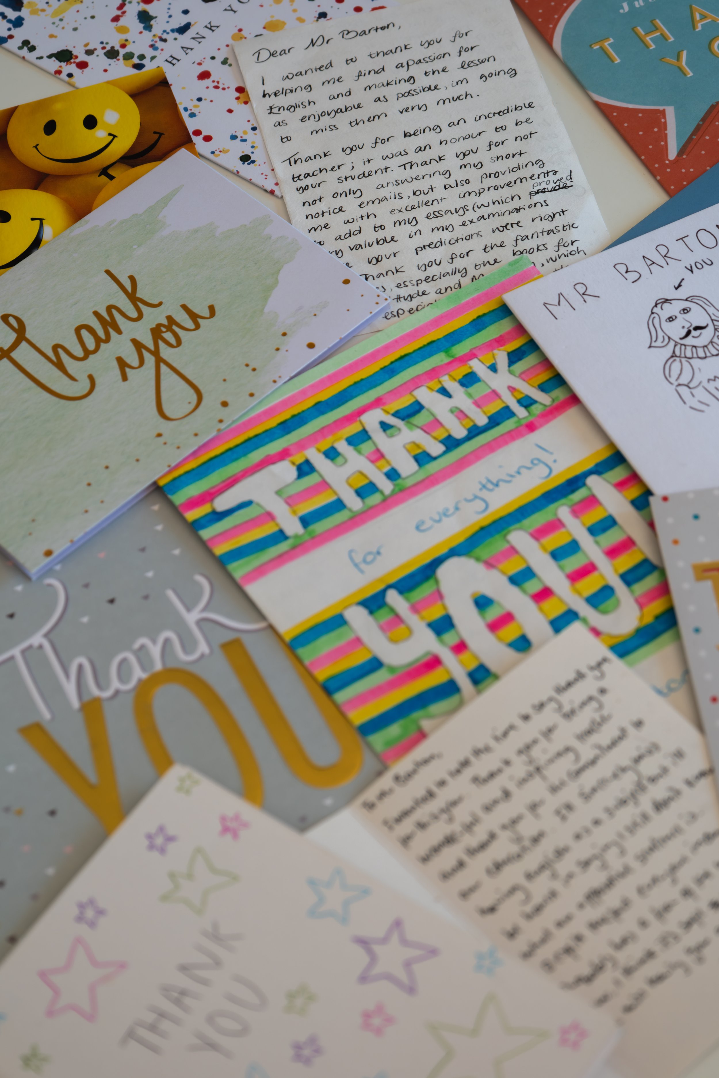 Collection of thank you cards, handwritten letters, colorful banners, and smiley face stress balls on a table.