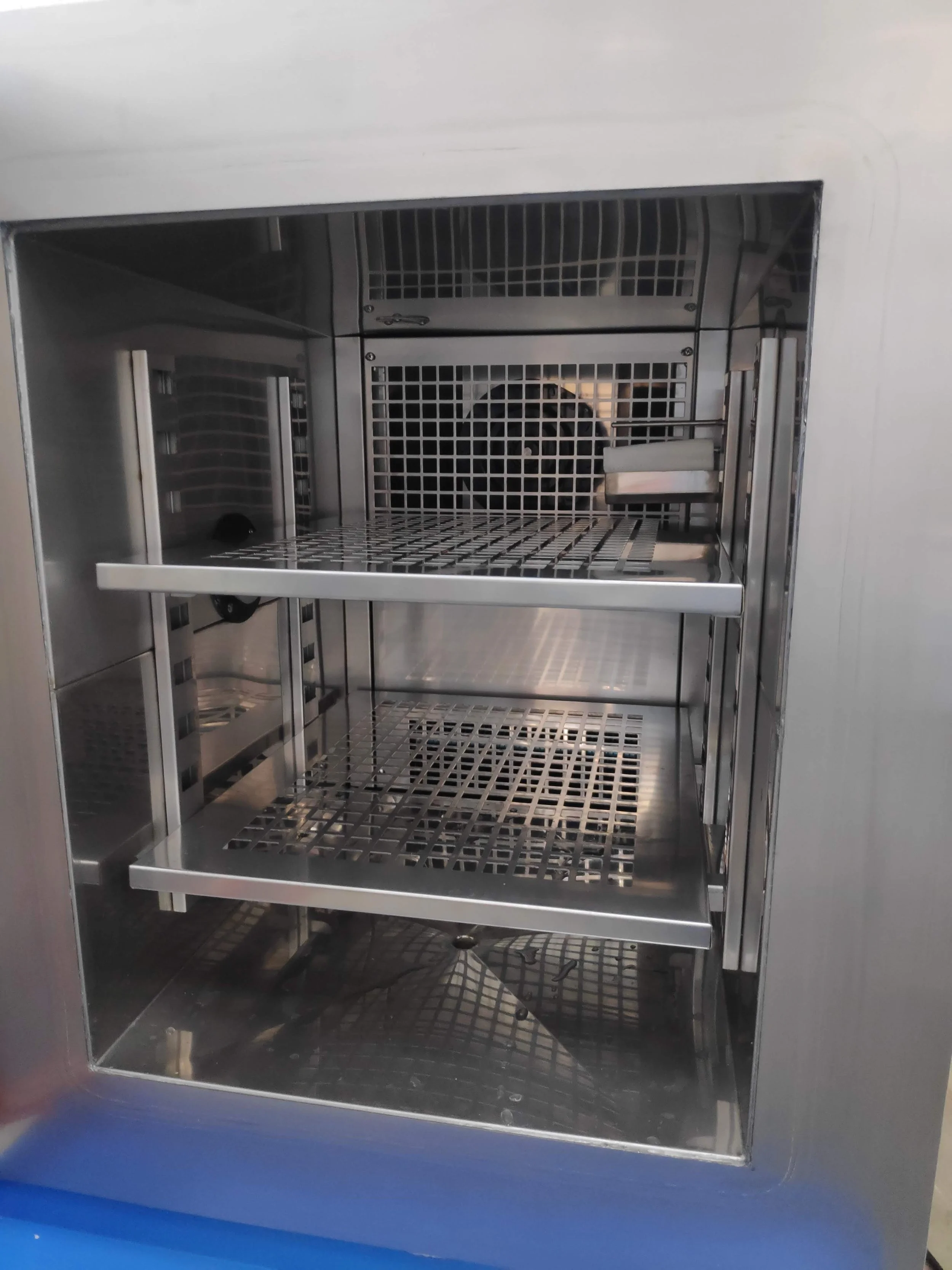 Empty stainless steel incubator with shelves and ventilation grid.