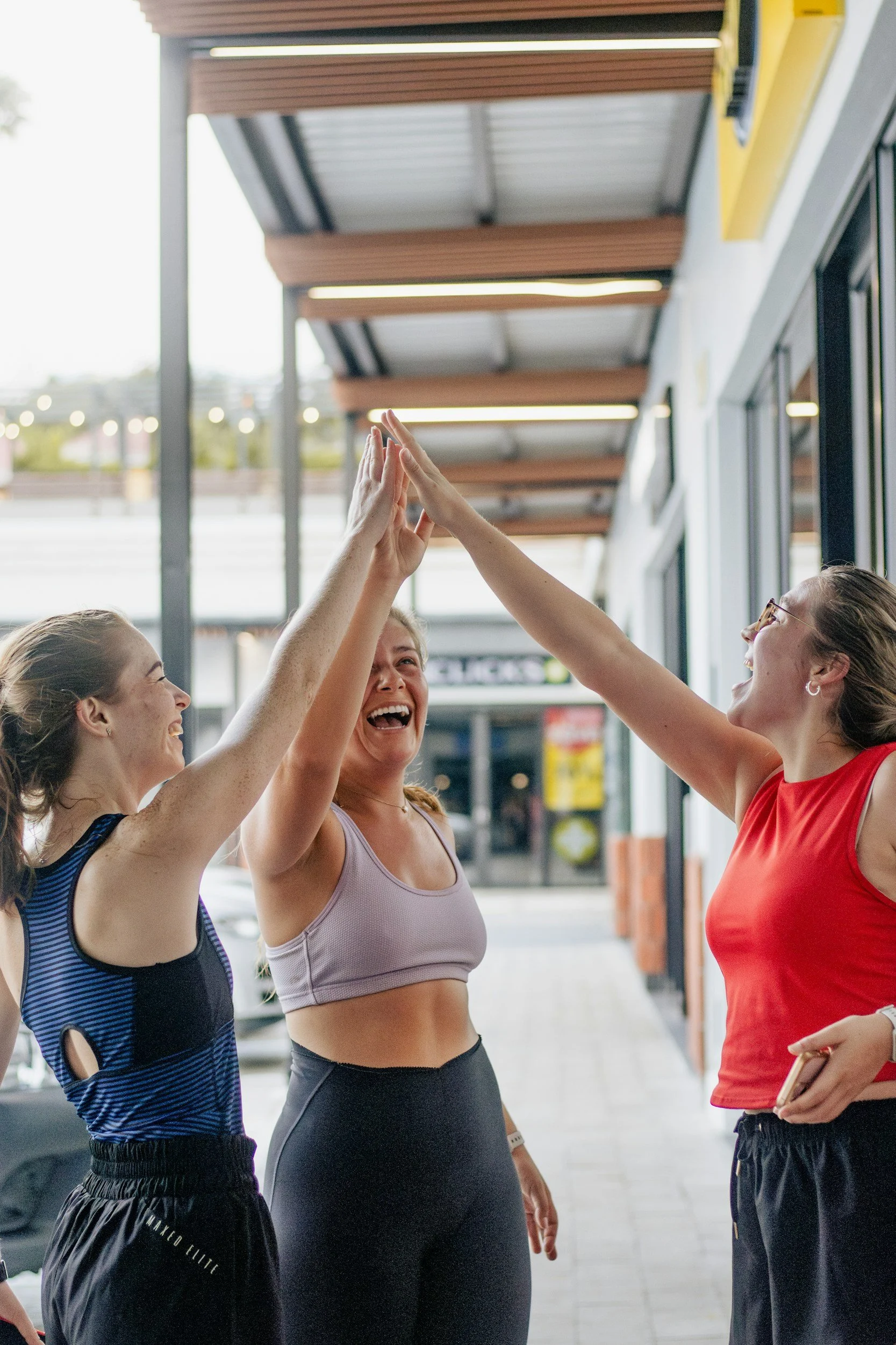 Four women in workout clothes giving each other high fives outdoors in front of a building.