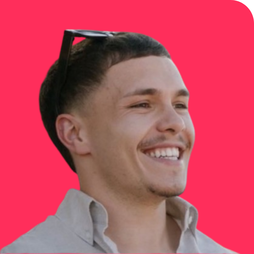 Close-up of smiling young man with sunglasses on his head against a pink background.