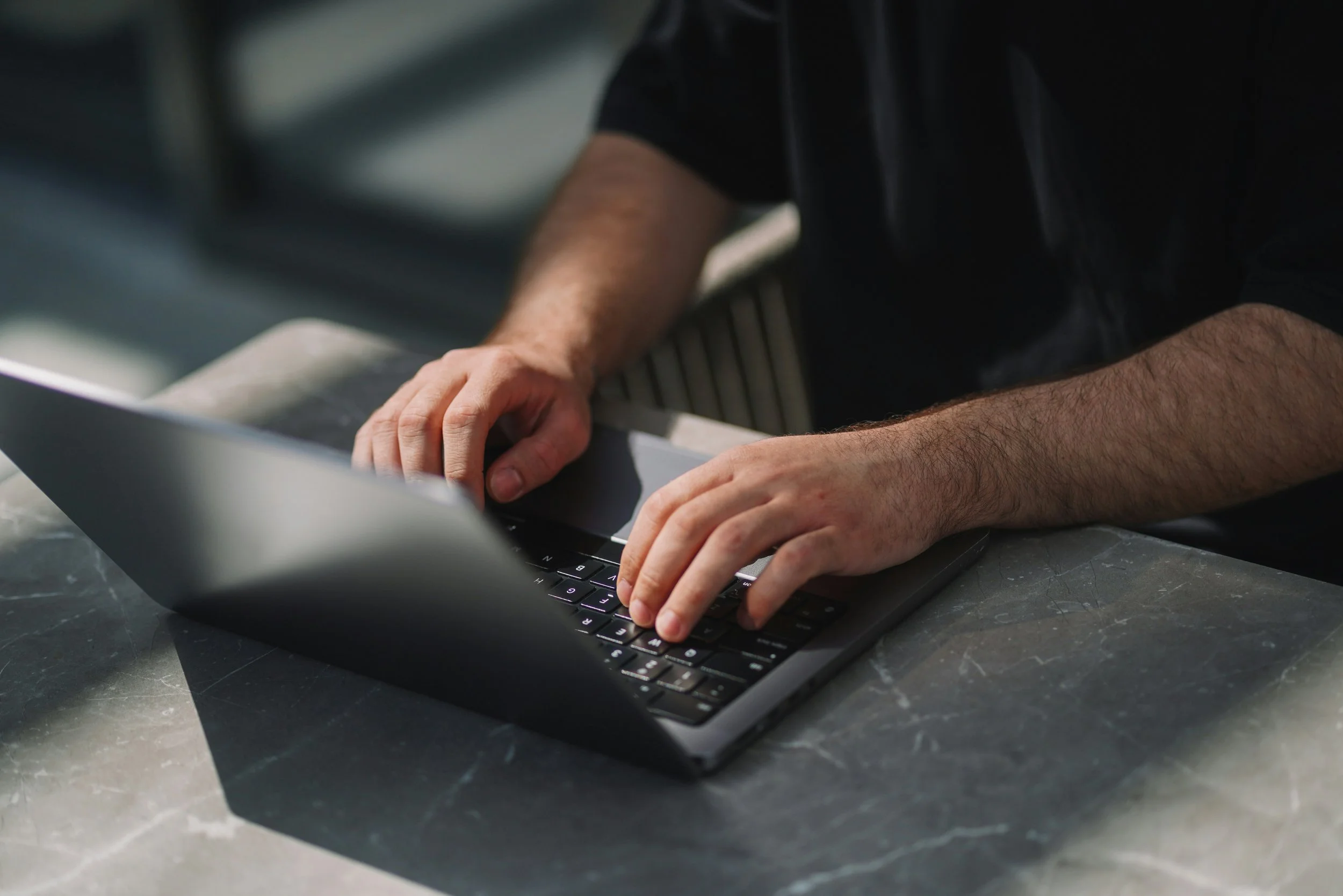 Person typing on a laptop computer with a dark marble surface around it.