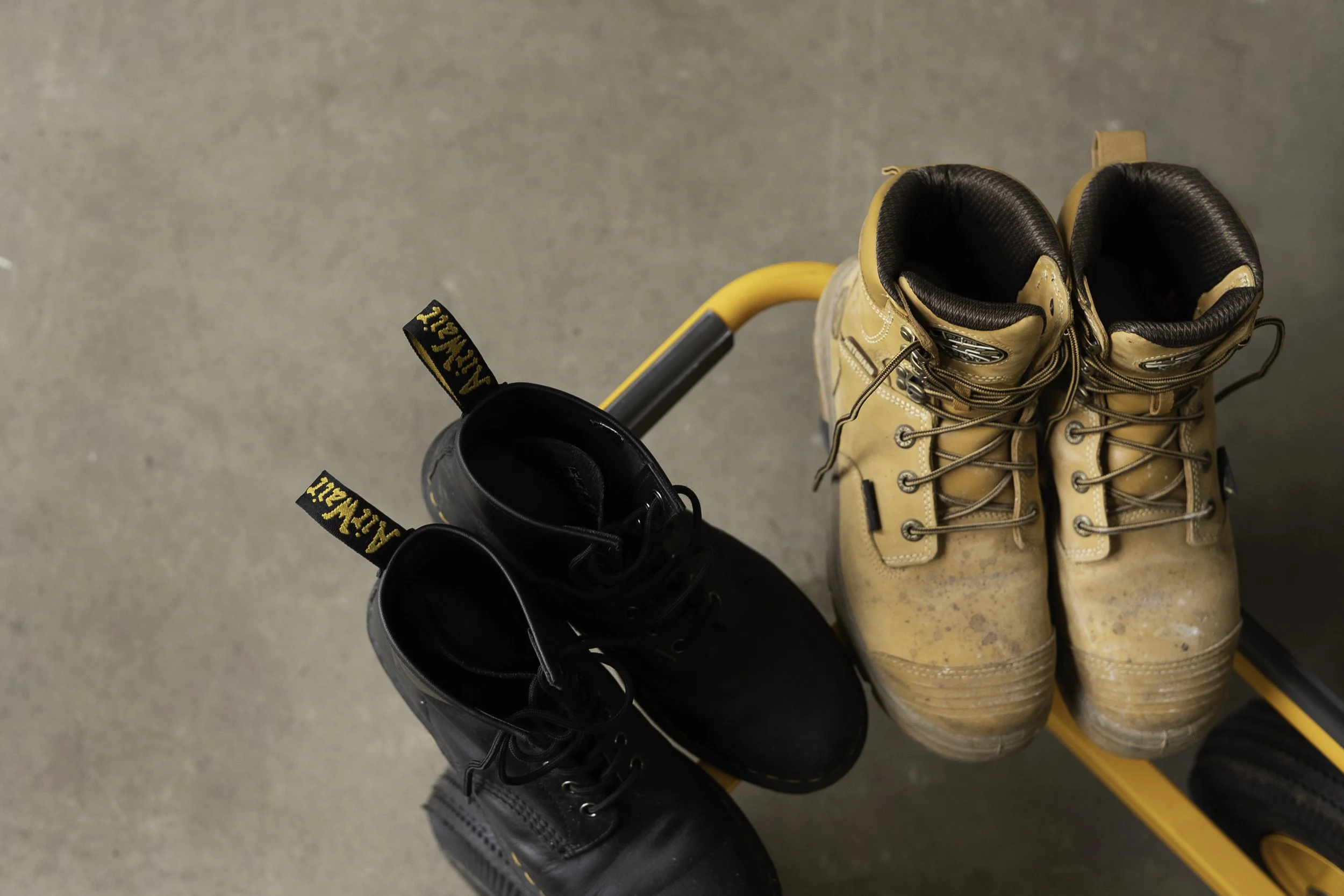A pair of black boots and a pair of tan work boots are placed on a yellow cart.