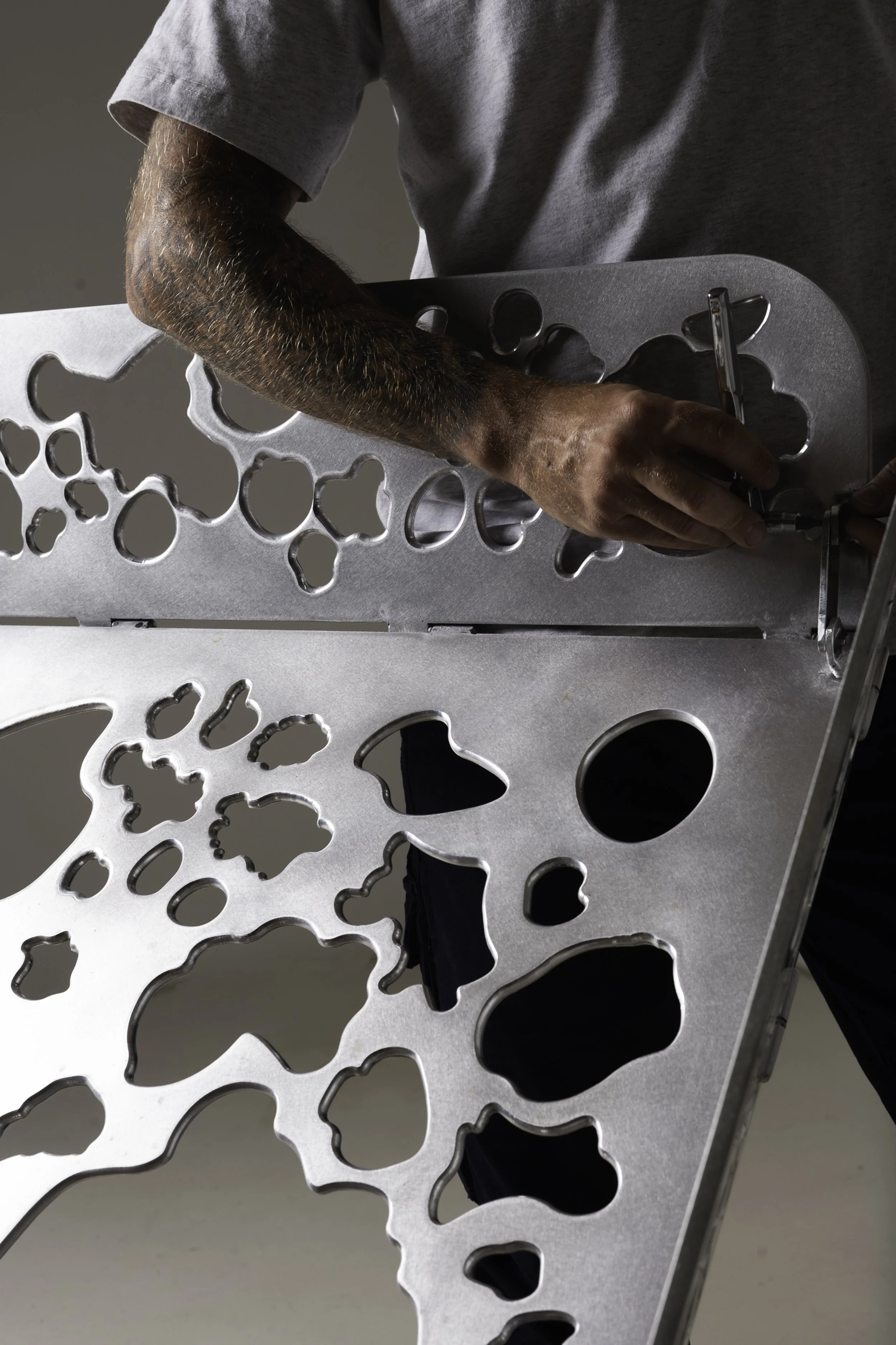 A man holding a metal workpiece with various shaped cutouts.
