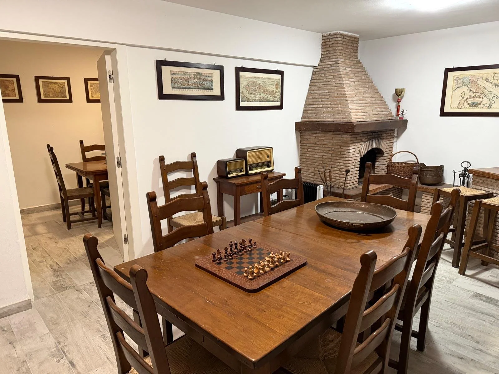 Sala da pranzo con tavolo in legno, sedie in legno, camino in mattoni, quadri su pareti e vetrina con oggetti decorativi.