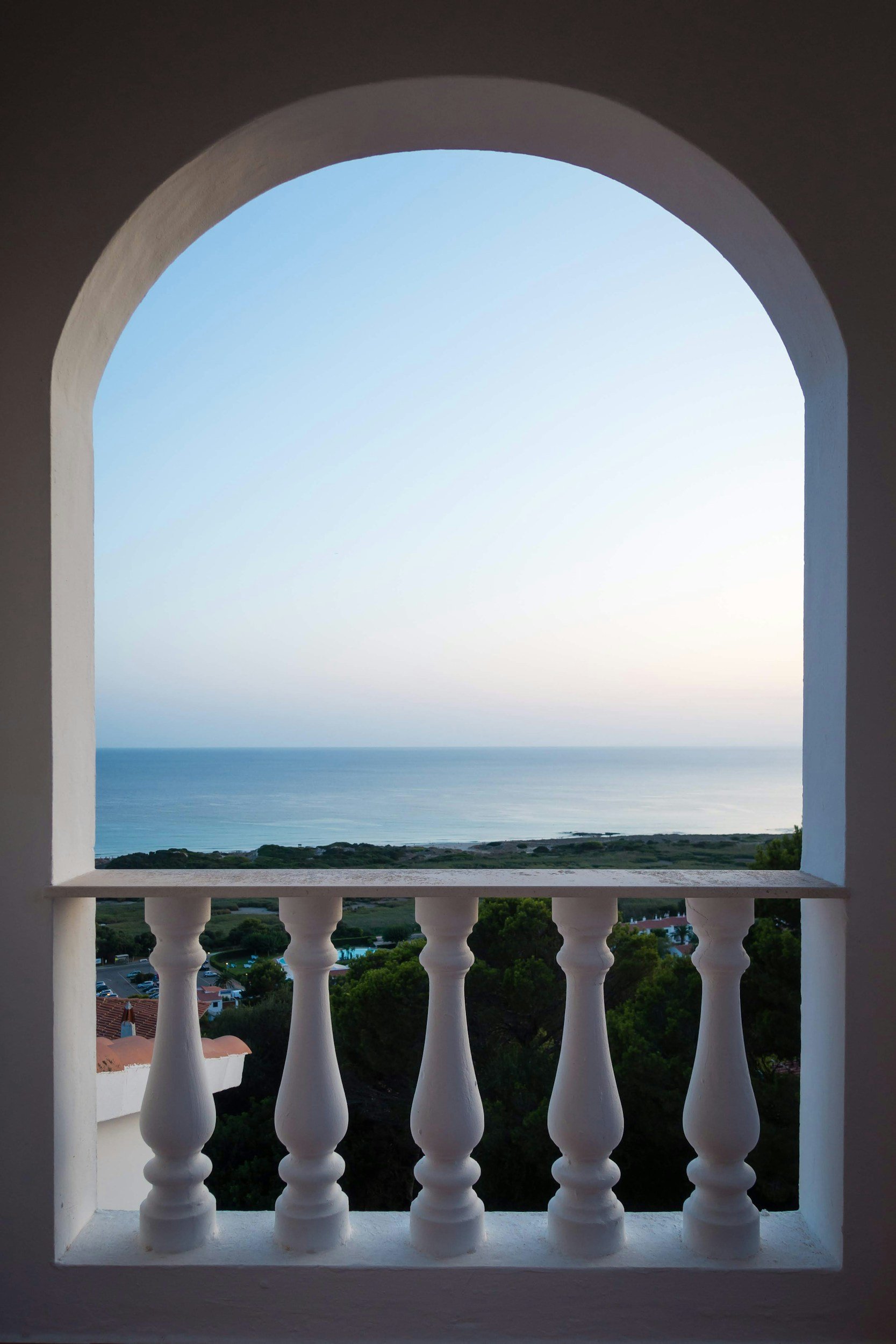 Sunset ocean view through an elegant balcony with white arches and a decorative balustrade