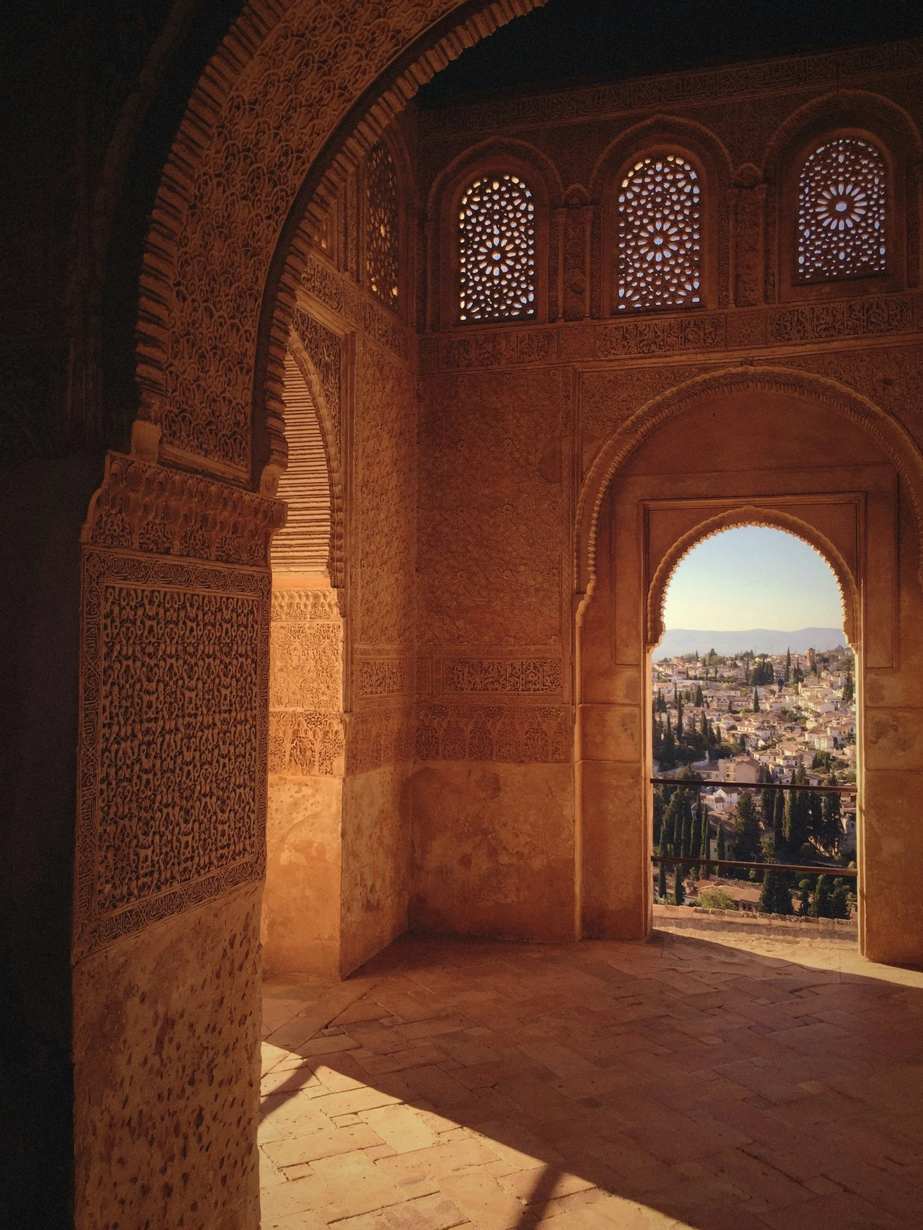 Interior of the Alhambra in Granada, Spain, with ornate arches, intricate carvings, lattice windows, and views of the surrounding hills