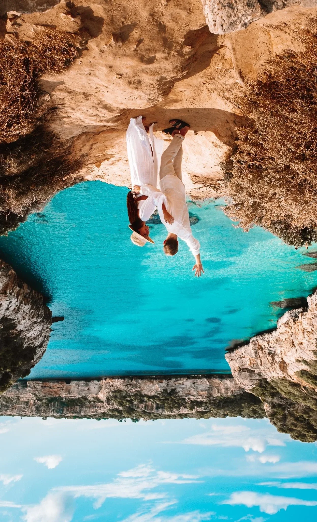 Couple overlooking a turquoise cove from a rocky viewpoint in Mallorca, Spain.