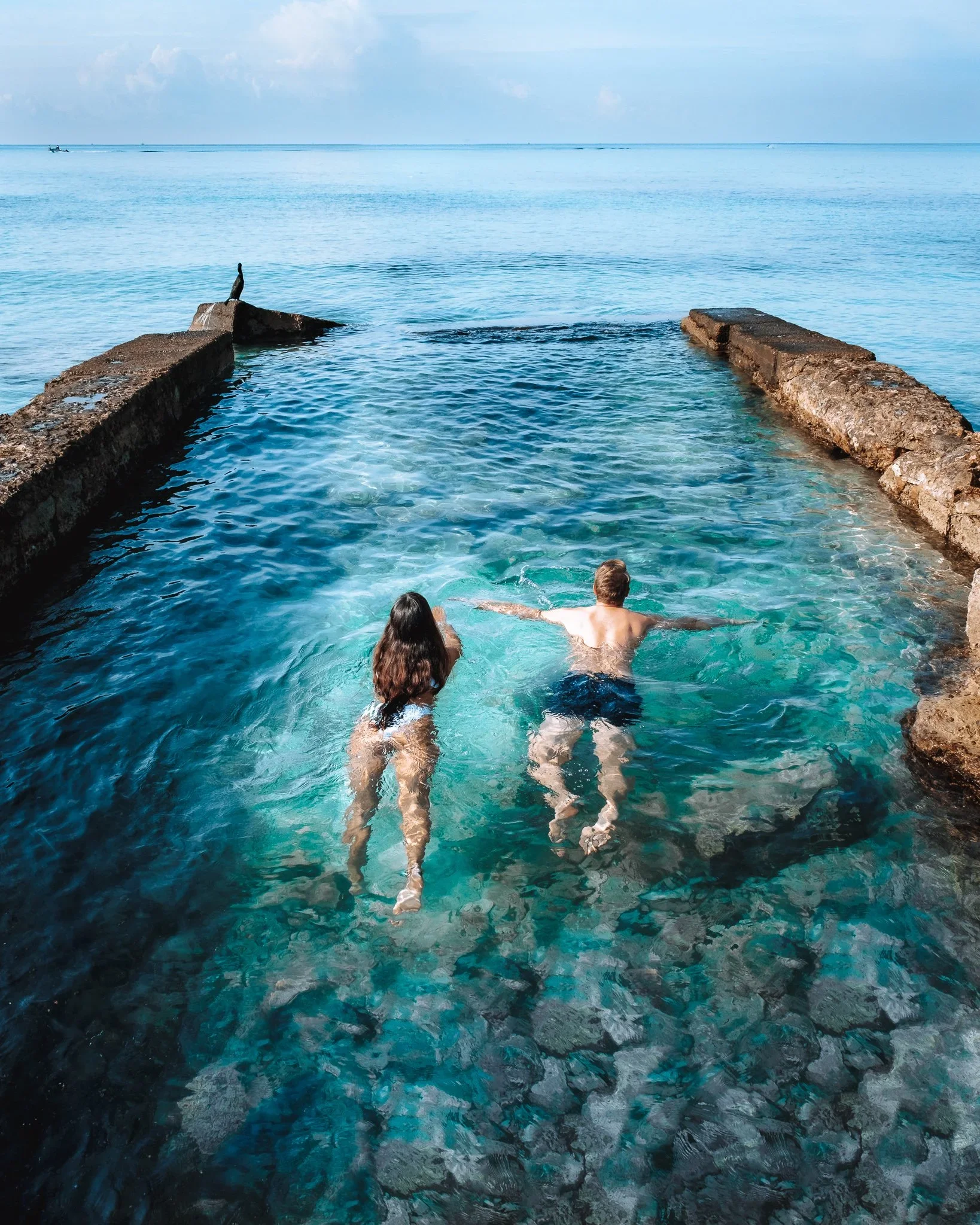 A couple swimming in a natural ocean pool overlooking the sea.