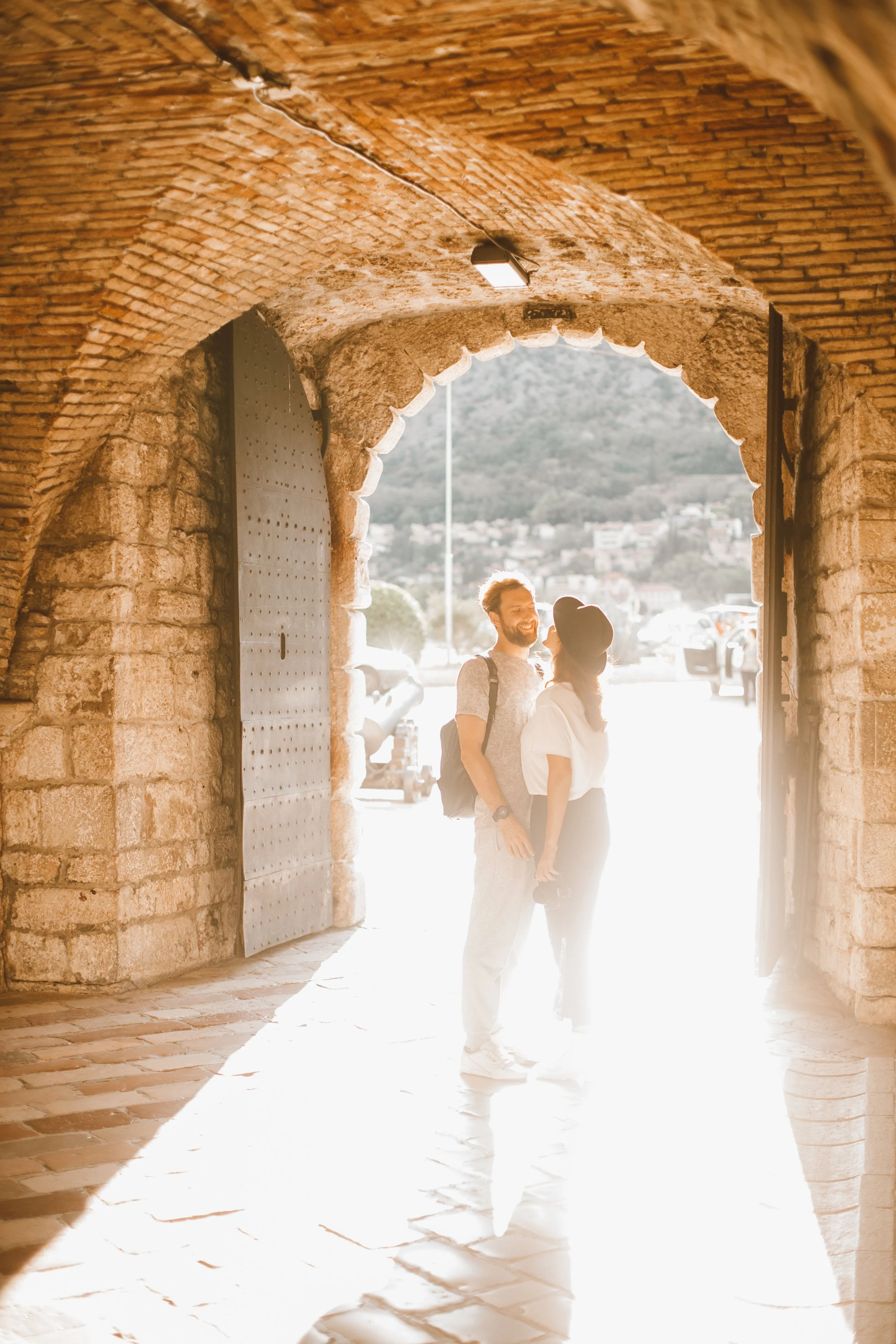 Couple embracing beneath a sunlit brick archway.
