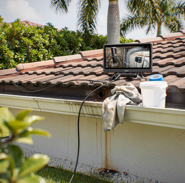 A monitor screen and white bucket sit on a gutter of a tile roof, with a rag draped over the edge near palm trees.