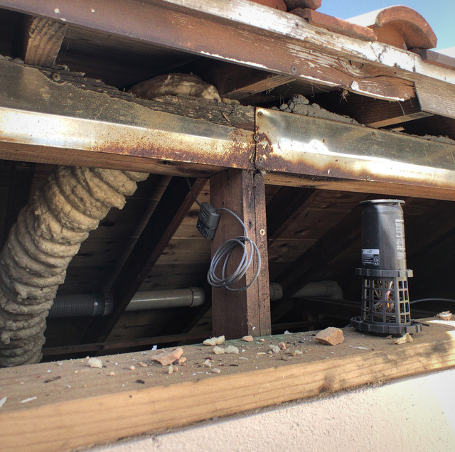 Deteriorated metal and wooden structure with rusty beams, coiled rope, drums, and scattered debris.