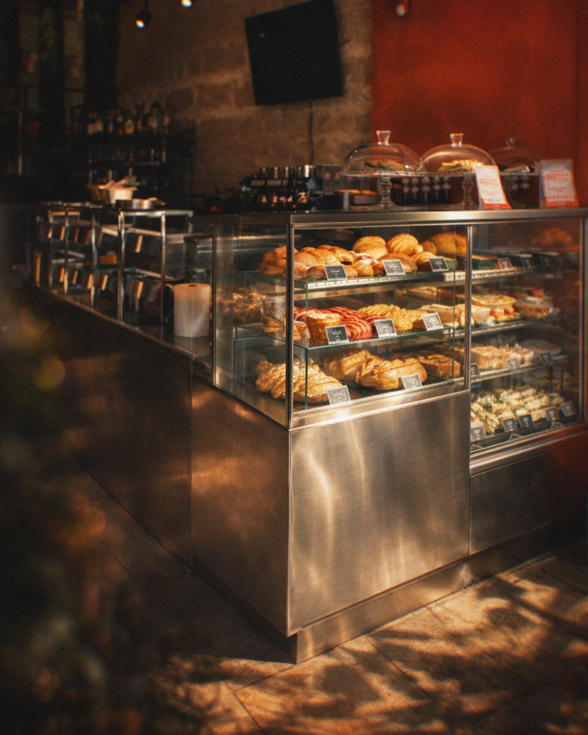 A glass display case filled with a variety of pastries, including croissants, with bakery labels in front of each item, situated in a dimly lit bakery or cafe setting.