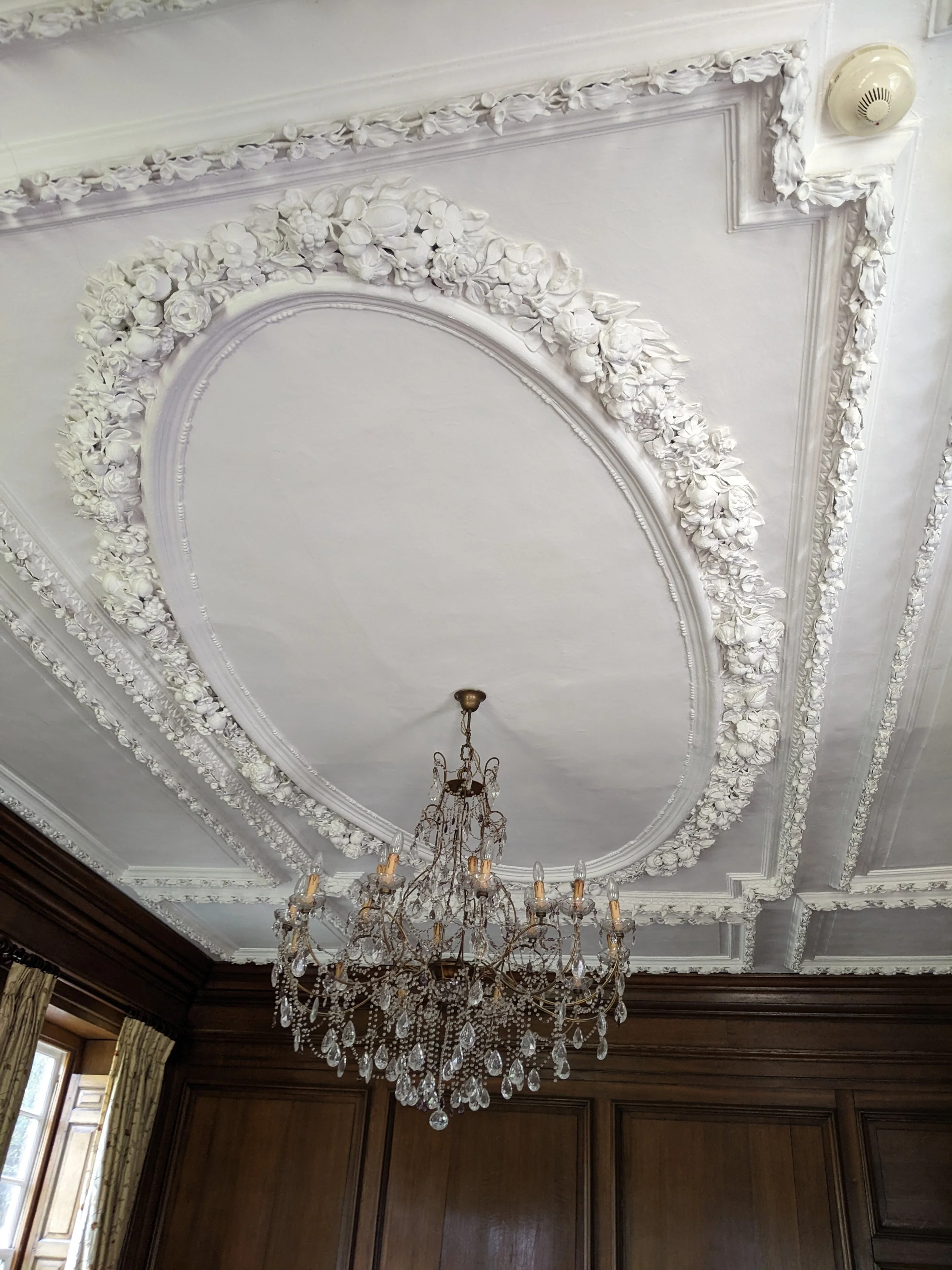 The ceiling features elaborate white plaster molding with floral and fruit patterns, and a large crystal chandelier hanging from the center.