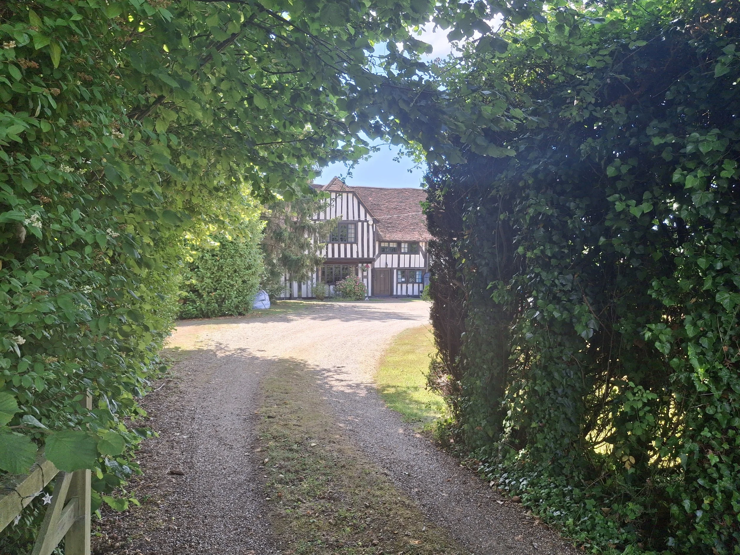 A gravel path leading to a house with traditional architecture, surrounded by lush green bushes and trees.