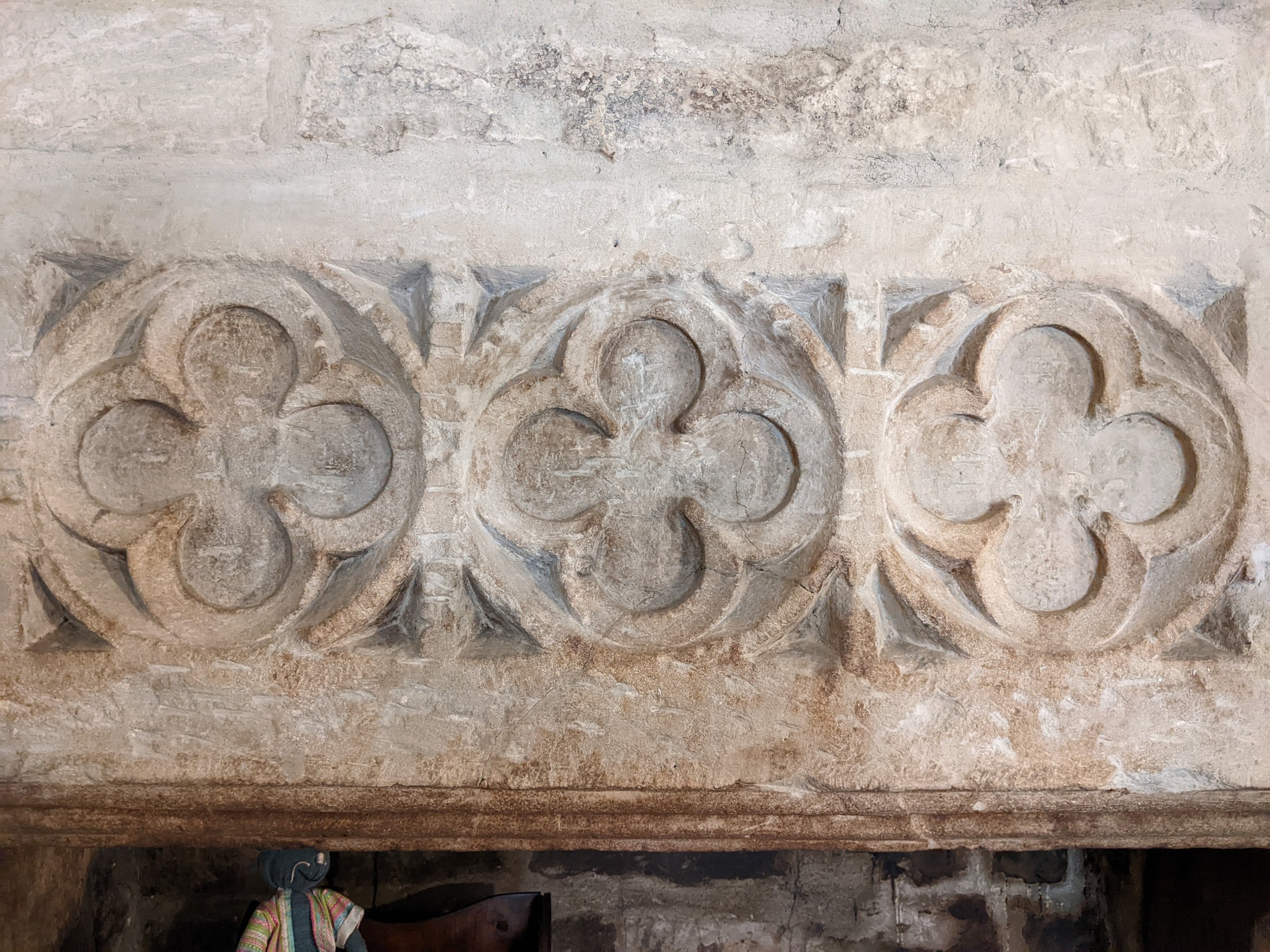A close-up view of carved stonework on a fire surround, featuring a decorative floral or scroll pattern. The stone appears aged and weathered.