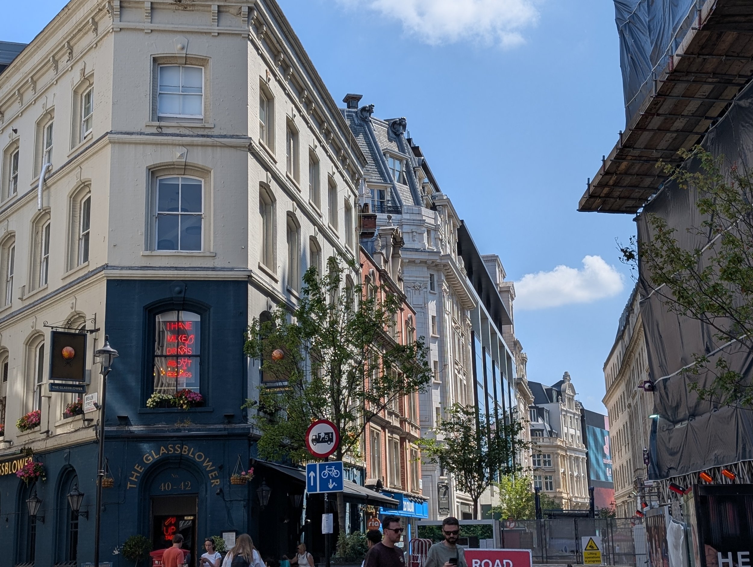 City street scene with historic buildings, pedestrians, street signs, and a partially covered pavement under construction.