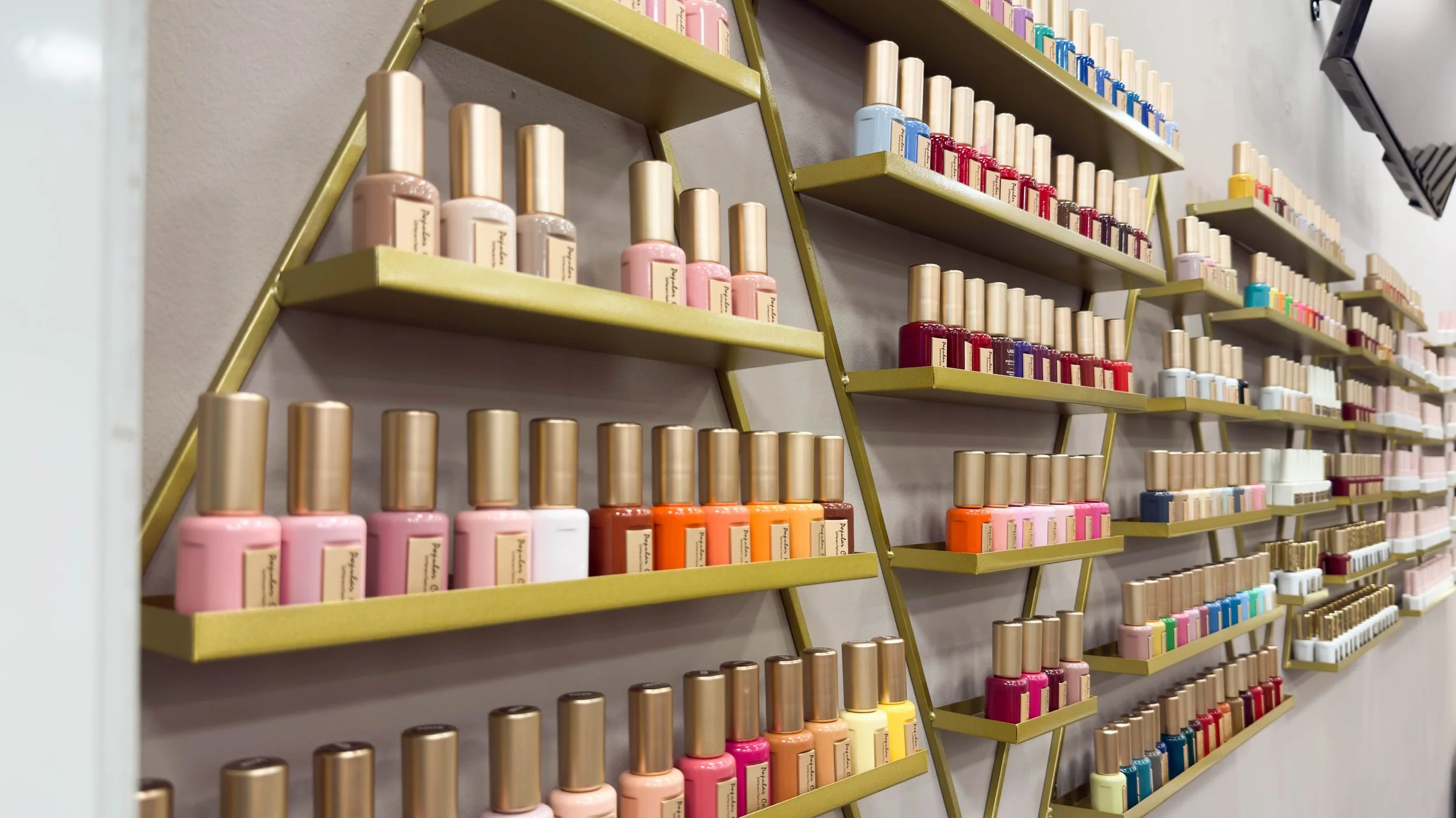 Regale mit verschiedenen Nagellacken in unterschiedlichen Farben, angeordnet auf goldfarbenen Regalböden im Laden.