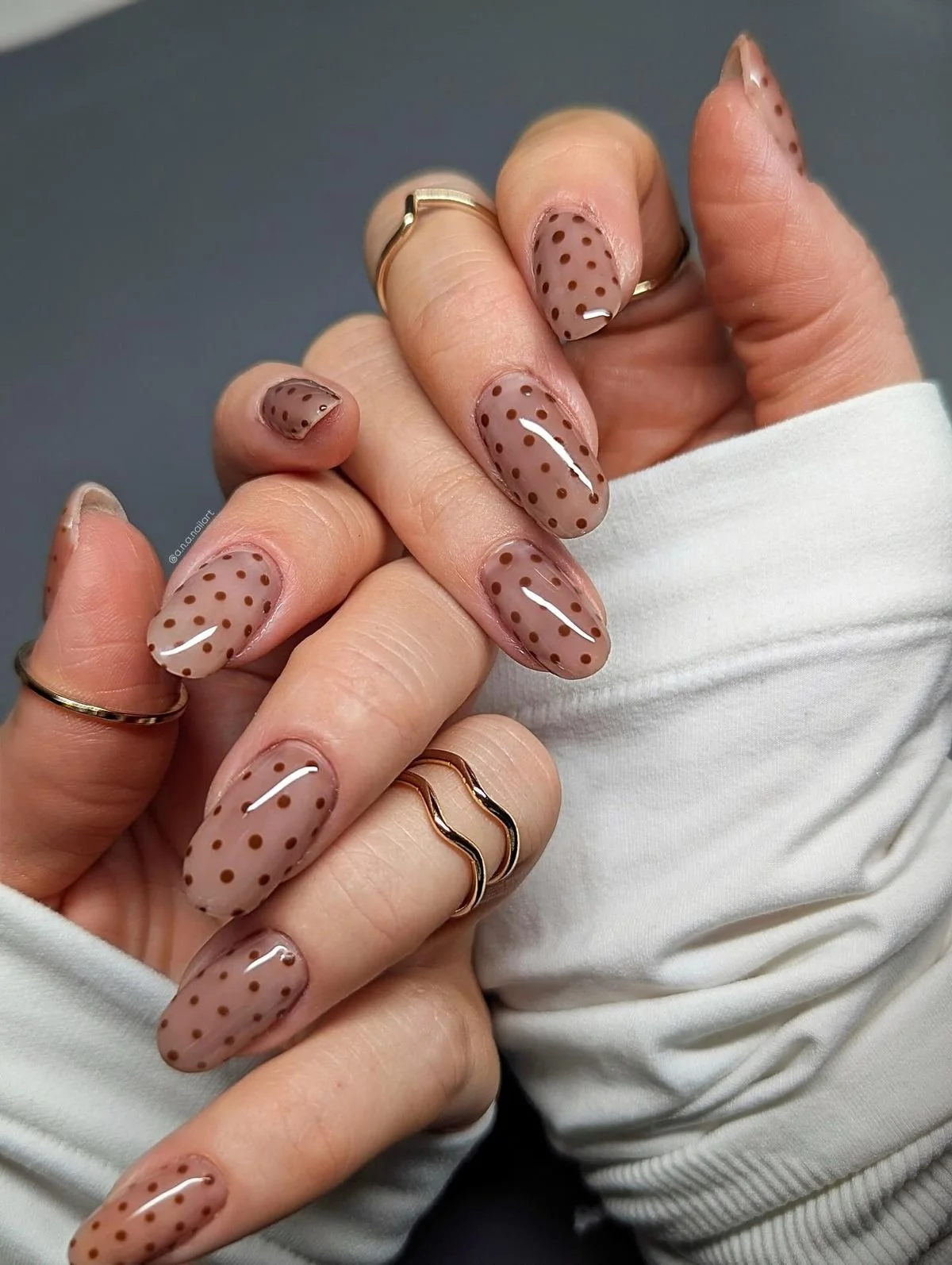 Nahaufnahme von Händen mit modellierten Fingernägeln, die braun mit kleinen dunklen Punkten sind.