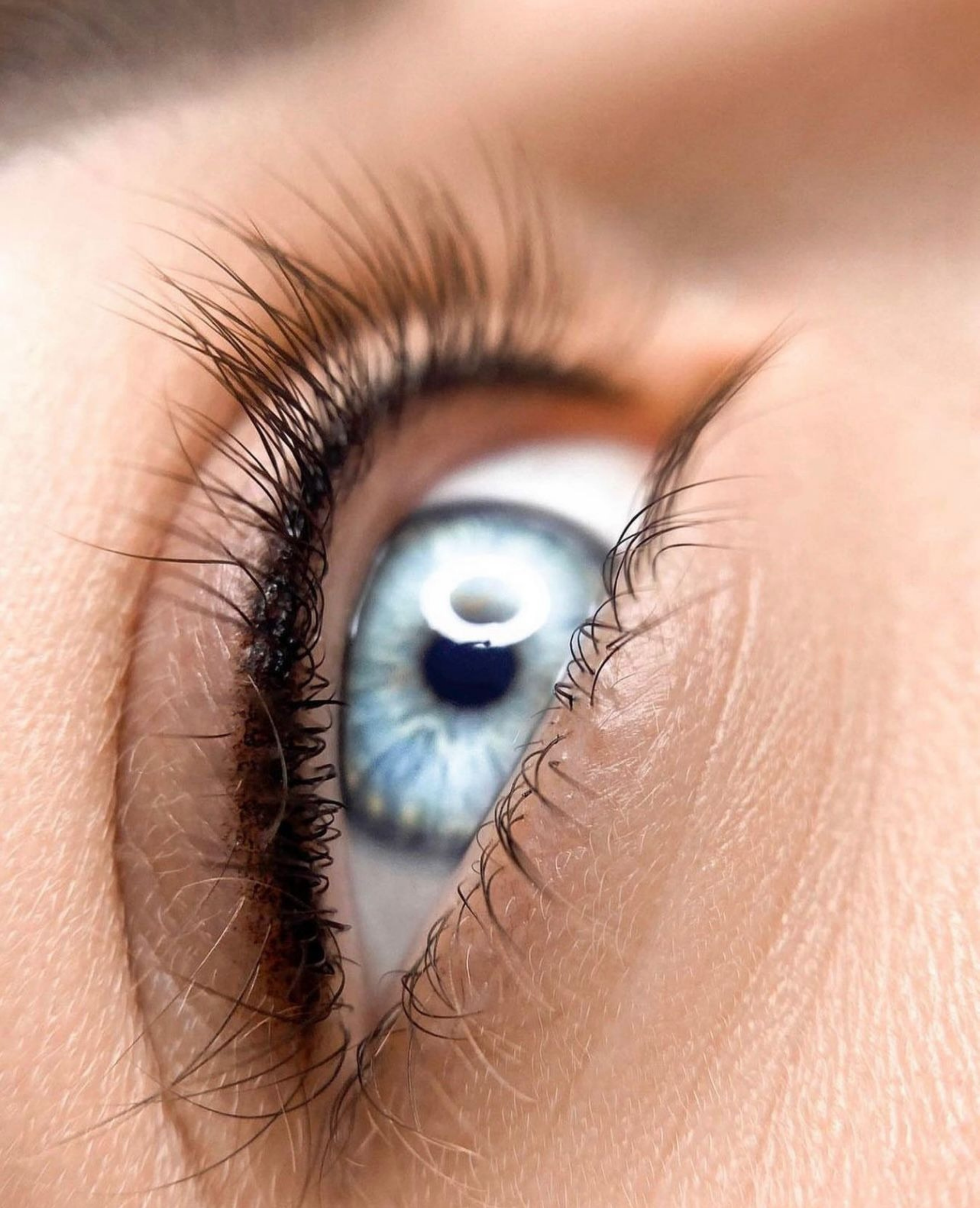 Nahaufnahme eines menschlichen Auges mit blauer Iris, lange Wimpern und Haut um das Auge