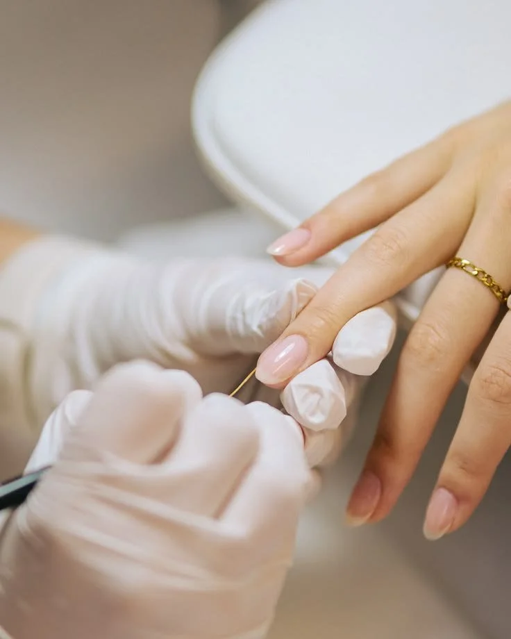 Eine Person erhält eine Nagelpflege oder eine Maniküre, während ein Nail Technician oder Kosmetikerin mit einem feinen Werkzeug an einem Nagel arbeitet.