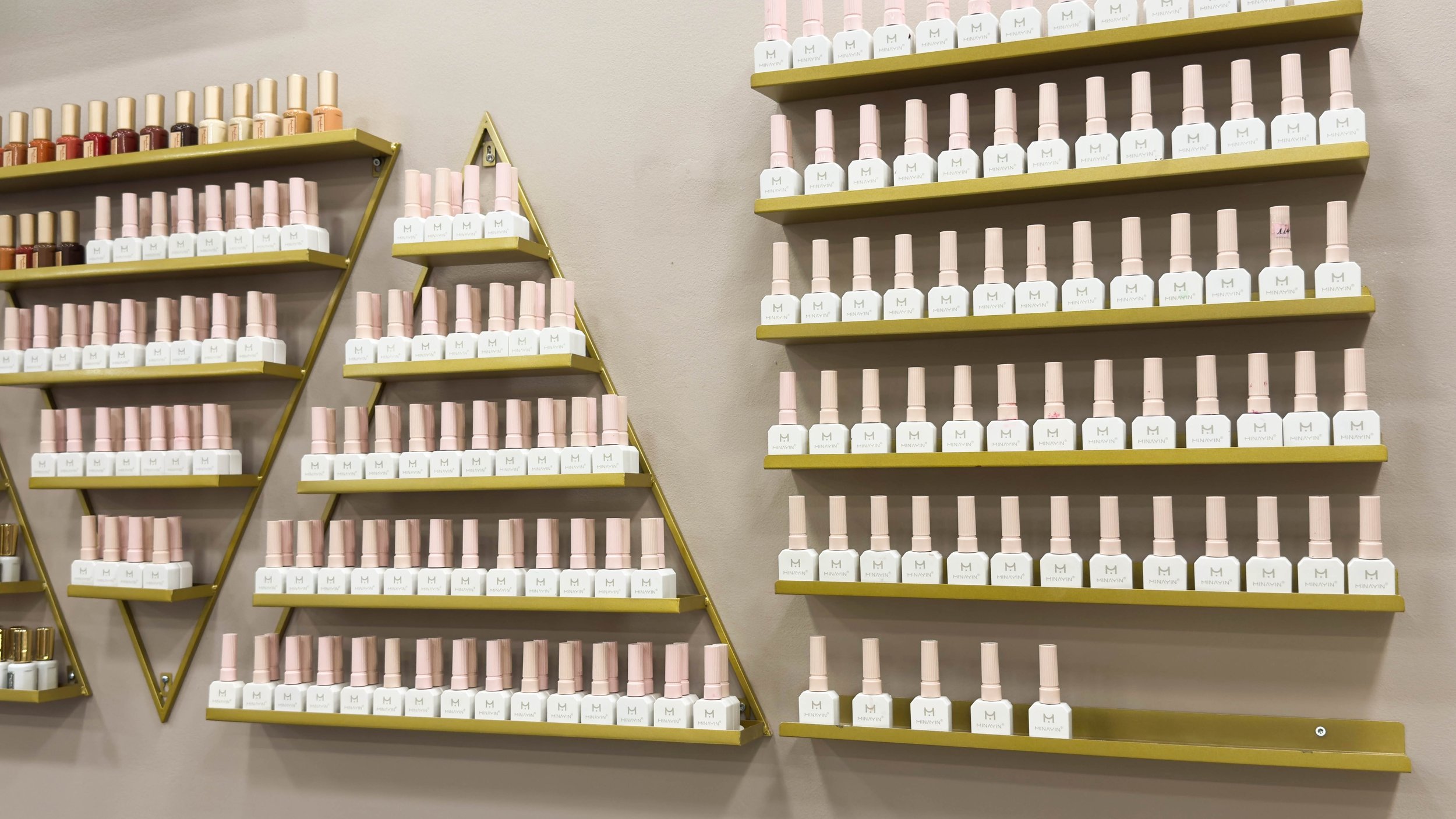 Mehrere Wandregale mit Nagellackflaschen, die in verschiedenen Farben angeordnet sind, in einem Nagelstudio oder Beauty-Salon.