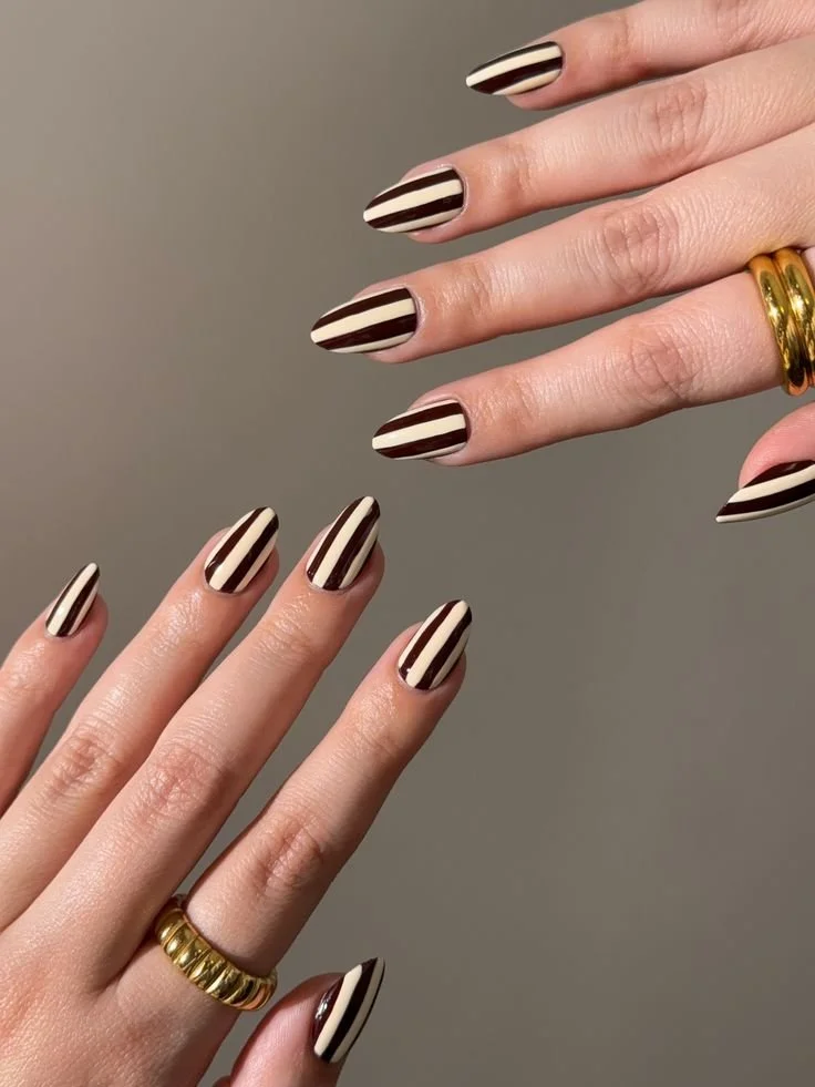 Nahaufnahme von zwei Händen mit gestreiftem, schwarzen und weißen Nagellack, beide Hände tragen goldene Ringe.