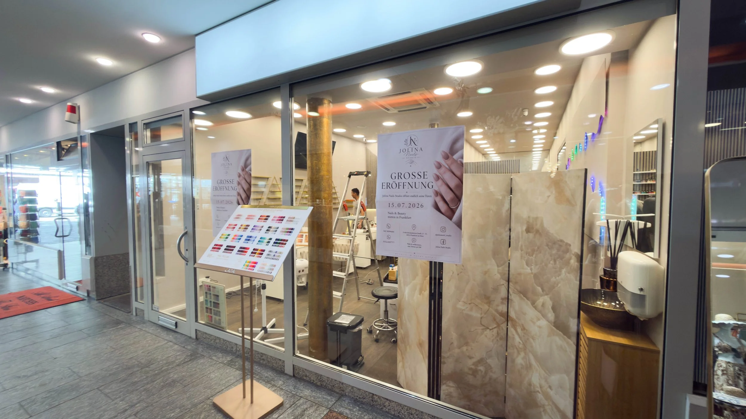 Eröffnungsfeier eines Nagelstudios mit Plakat, das den Termin 15.07.2026 für die große Eröffnung ankündigt.