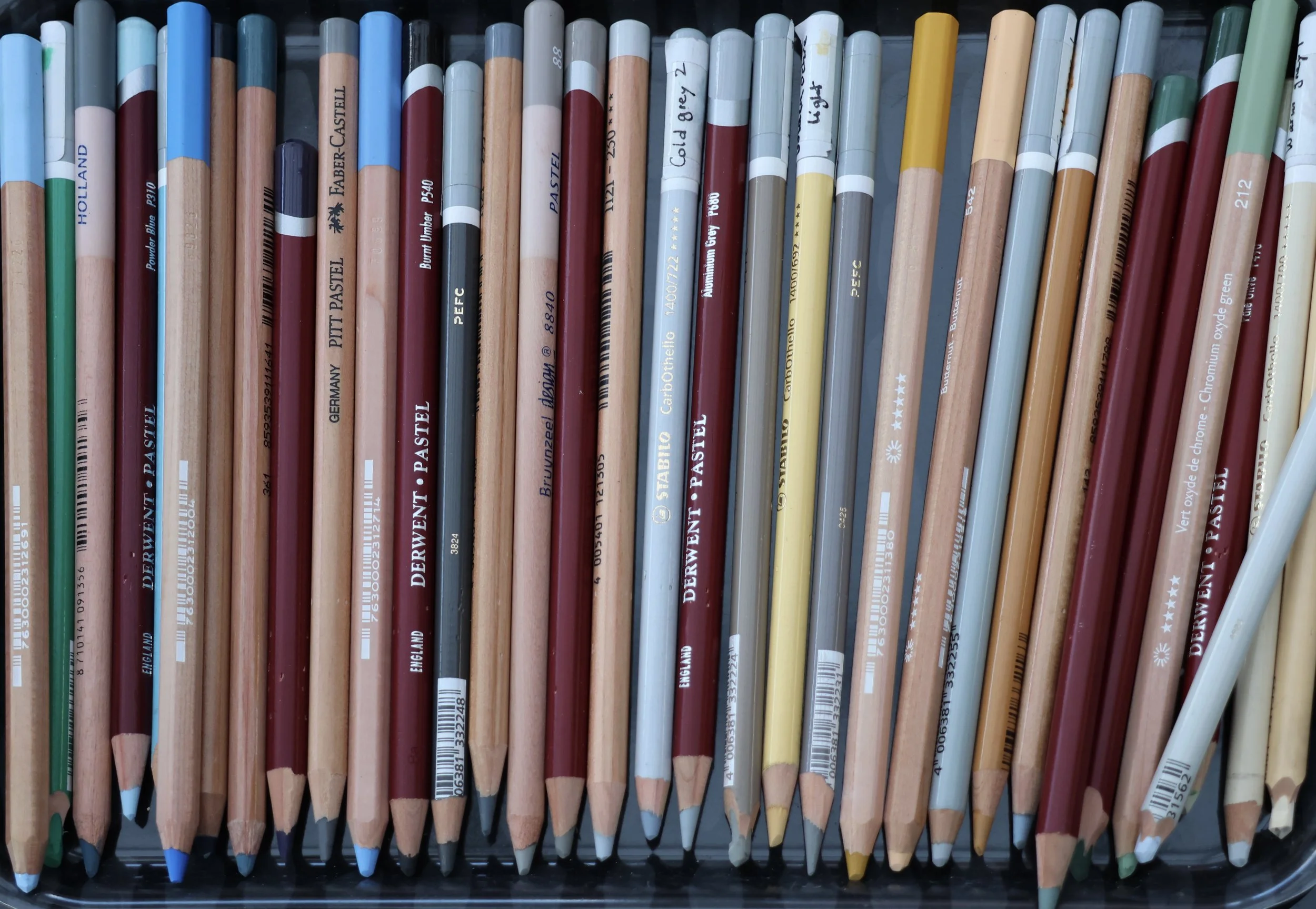 A collection of soft pastel pencils of different brands with various shades of blue, red, yellow, green, gray, and beige.