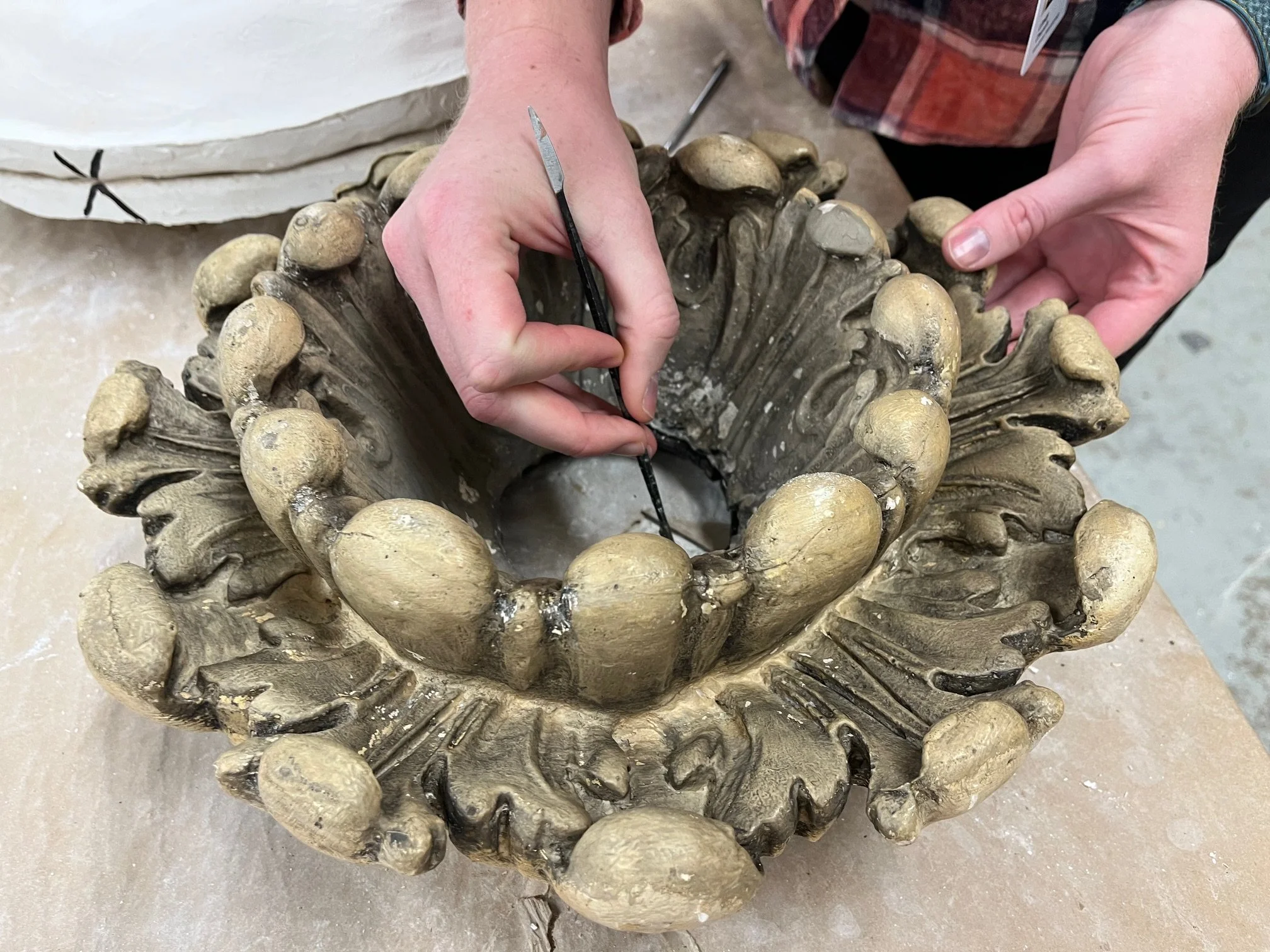 Close-up of a person restoring a decorative element of the historic theater with a circular design and petal-like features. The person is holding a small tool and working on the sculptural element.