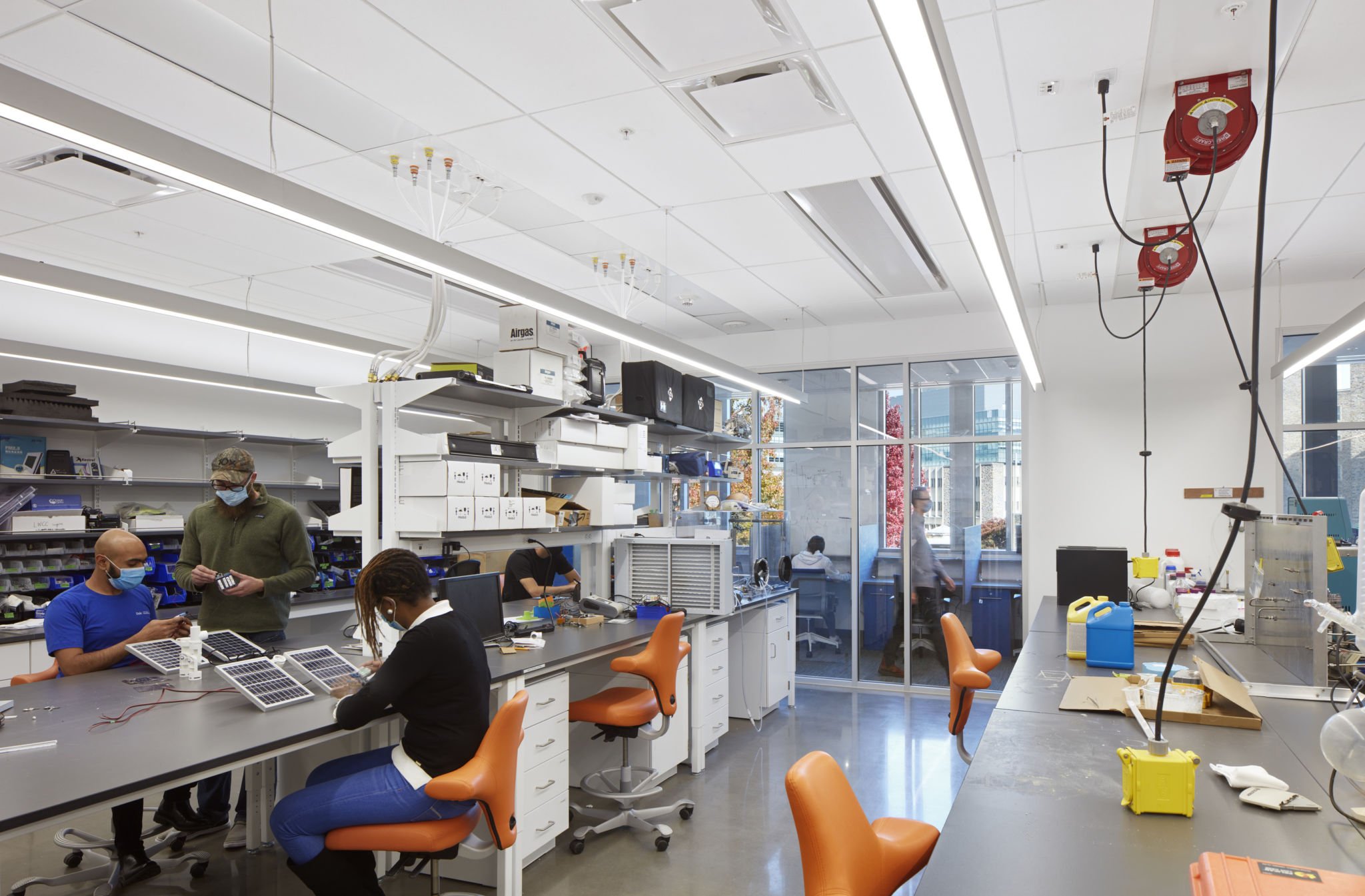 People working on projects in a bright, modern laboratory with scientific equipment, white shelving, and large windows.