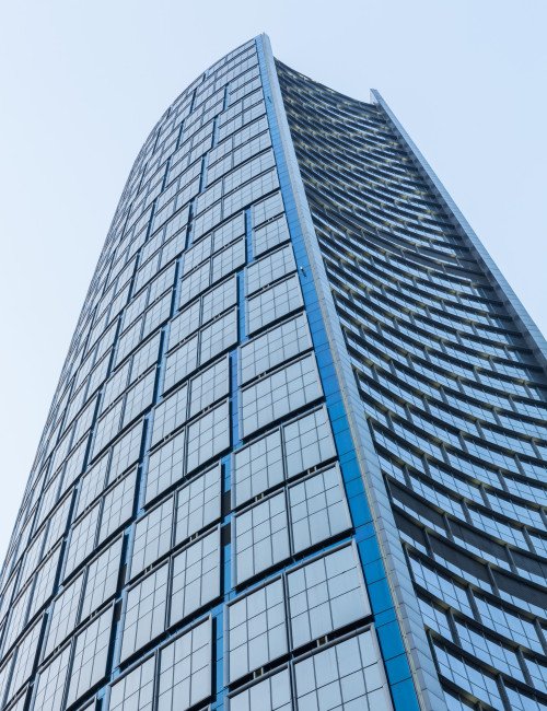 Modern skyscraper with glass windows and curved design against a light blue sky.