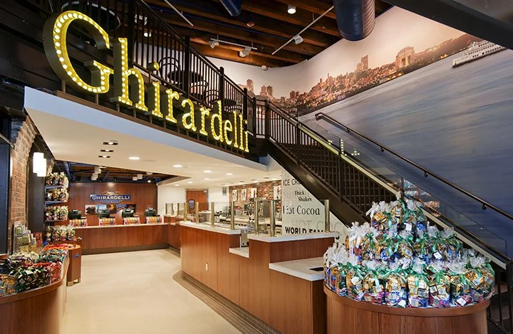 Ghirardelli chocolate shop interior with a large illuminated sign, a counter area with chocolate products.