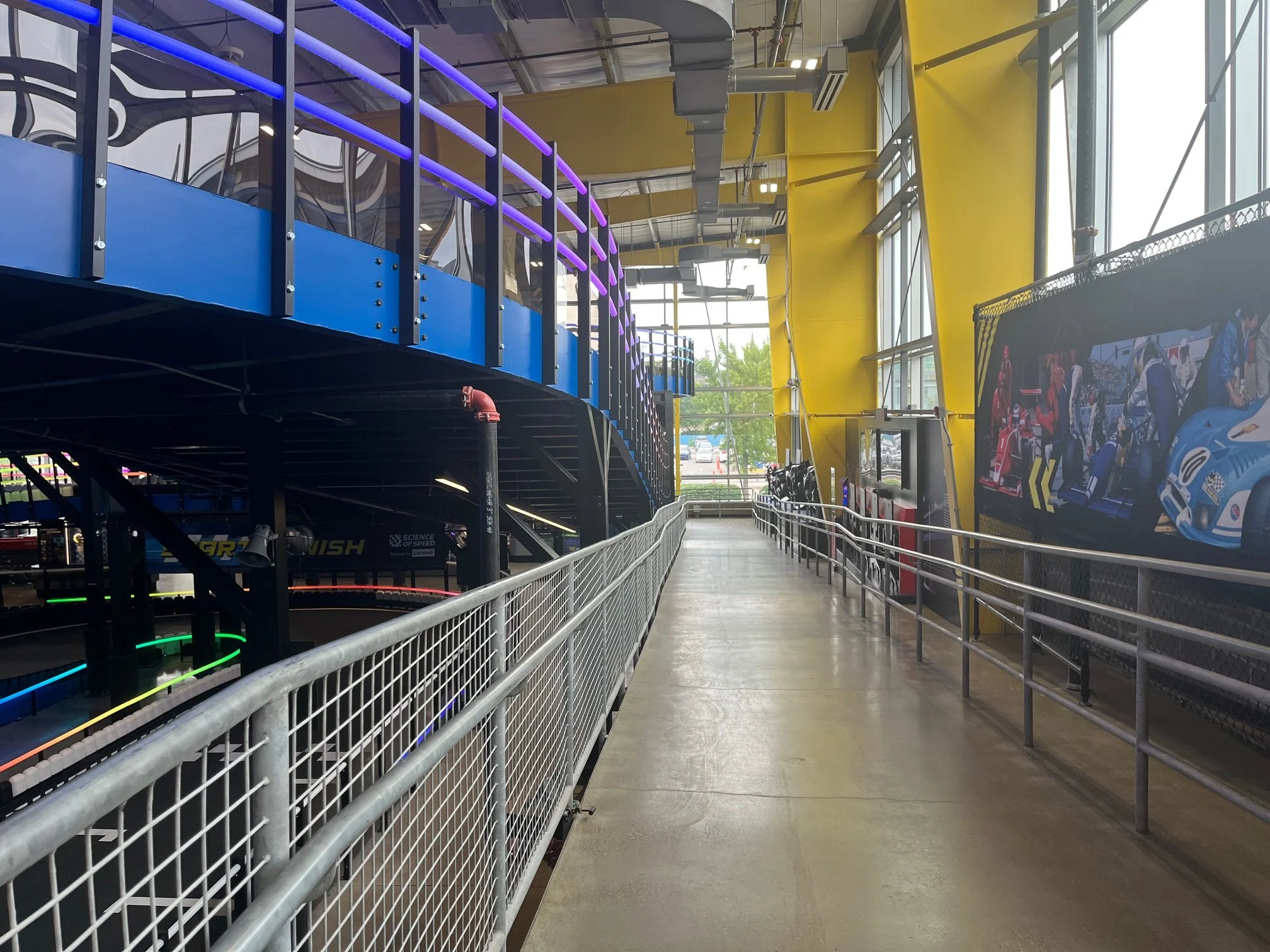 Indoor science center with a blue and black elevated track, neon purple and yellow accents, and a large mural of racing cars.