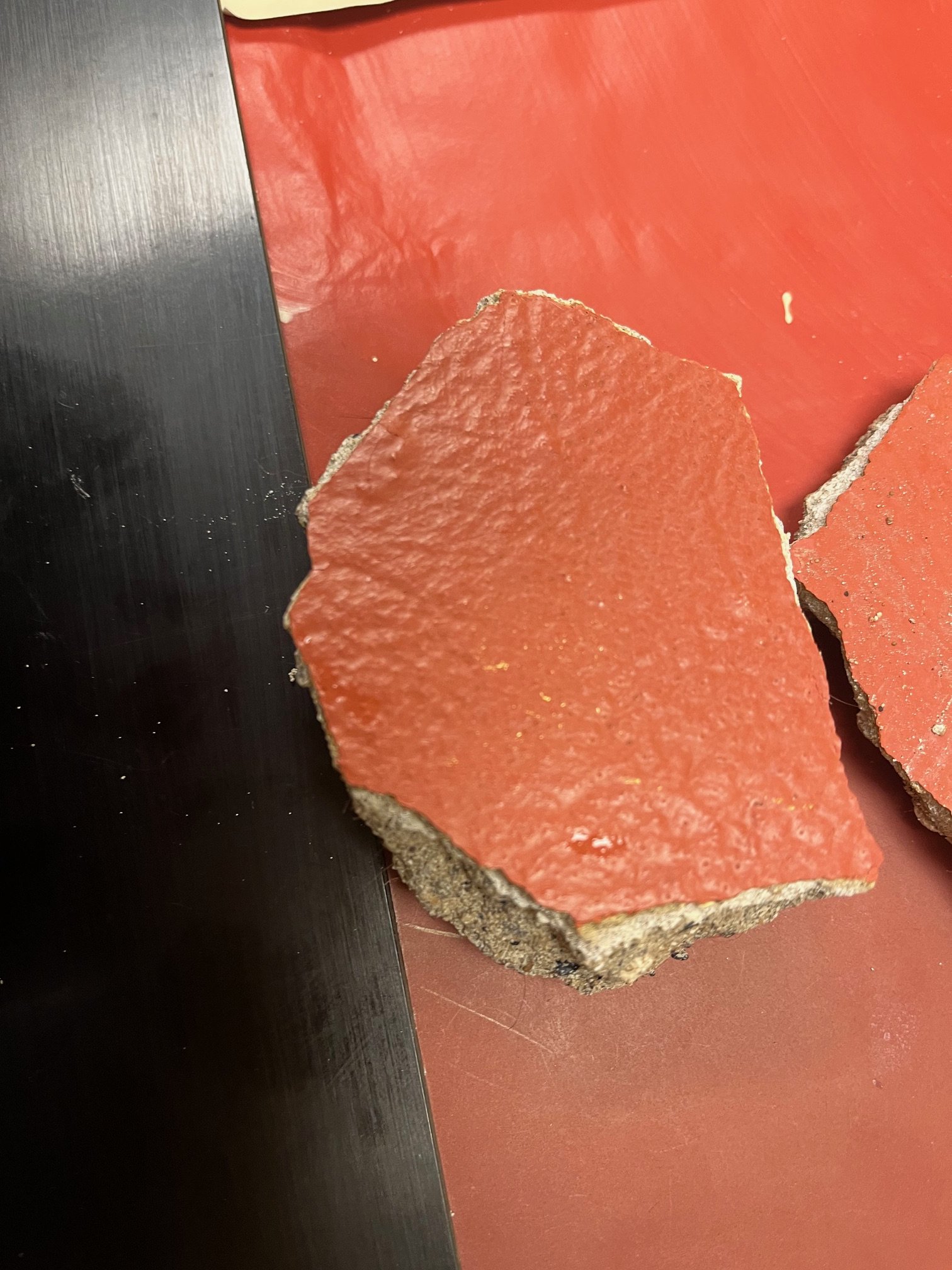 Close-up of smashed orange-red tile with rough edges placed on a dark surface.