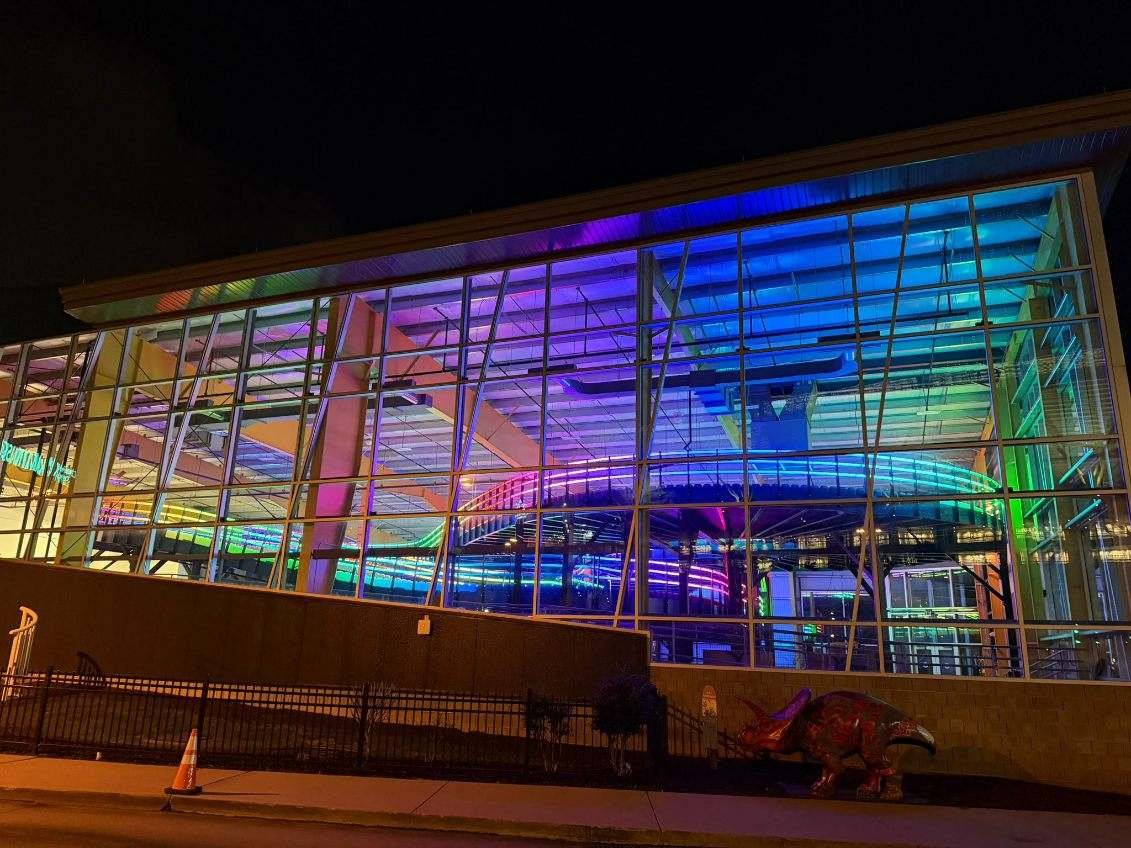 A modern building with large glass windows illuminated with colorful neon lights at night.