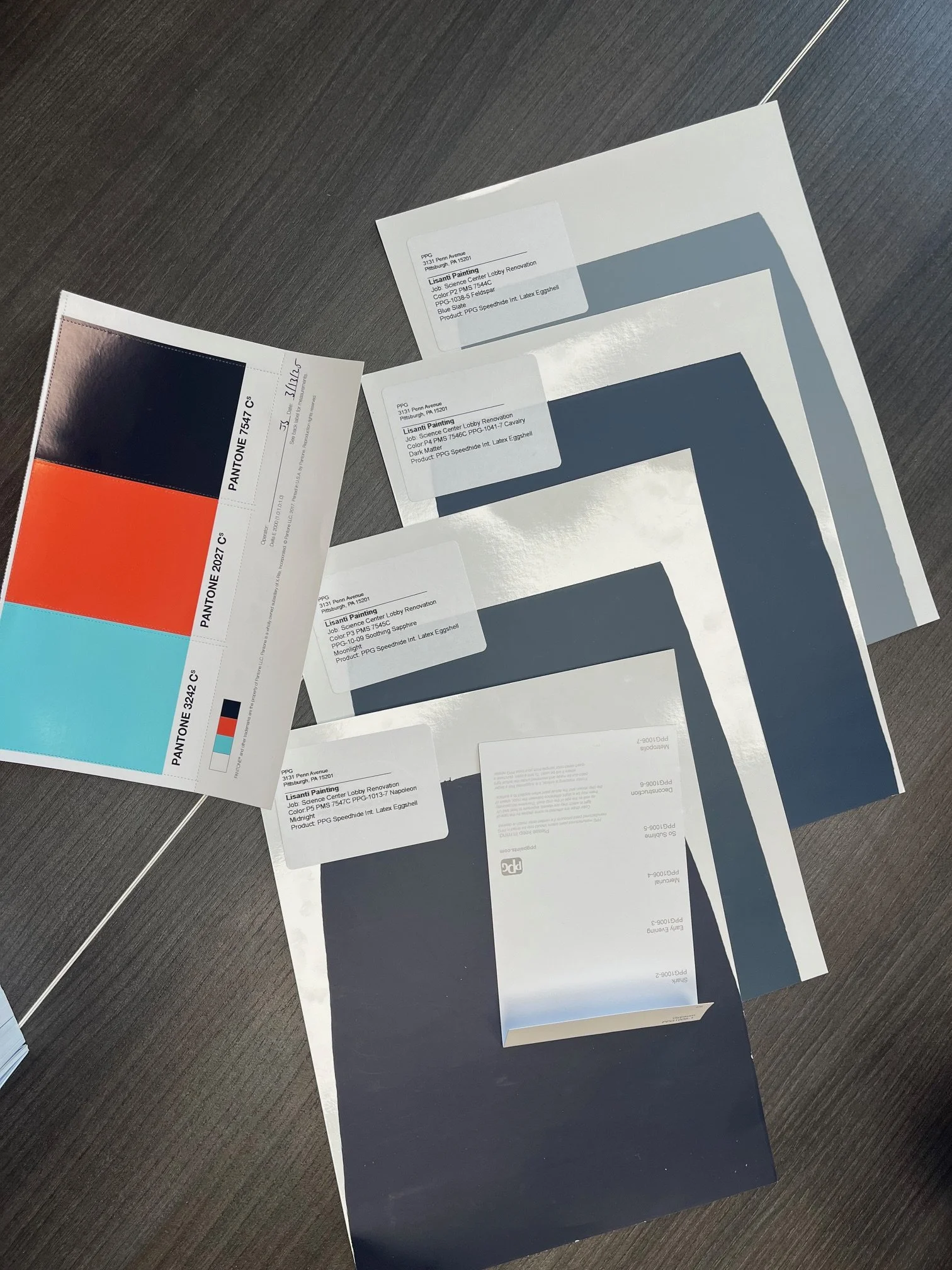 Color swatches and printed color labels on a dark grey surface, with some labels showing paint color names and codes.