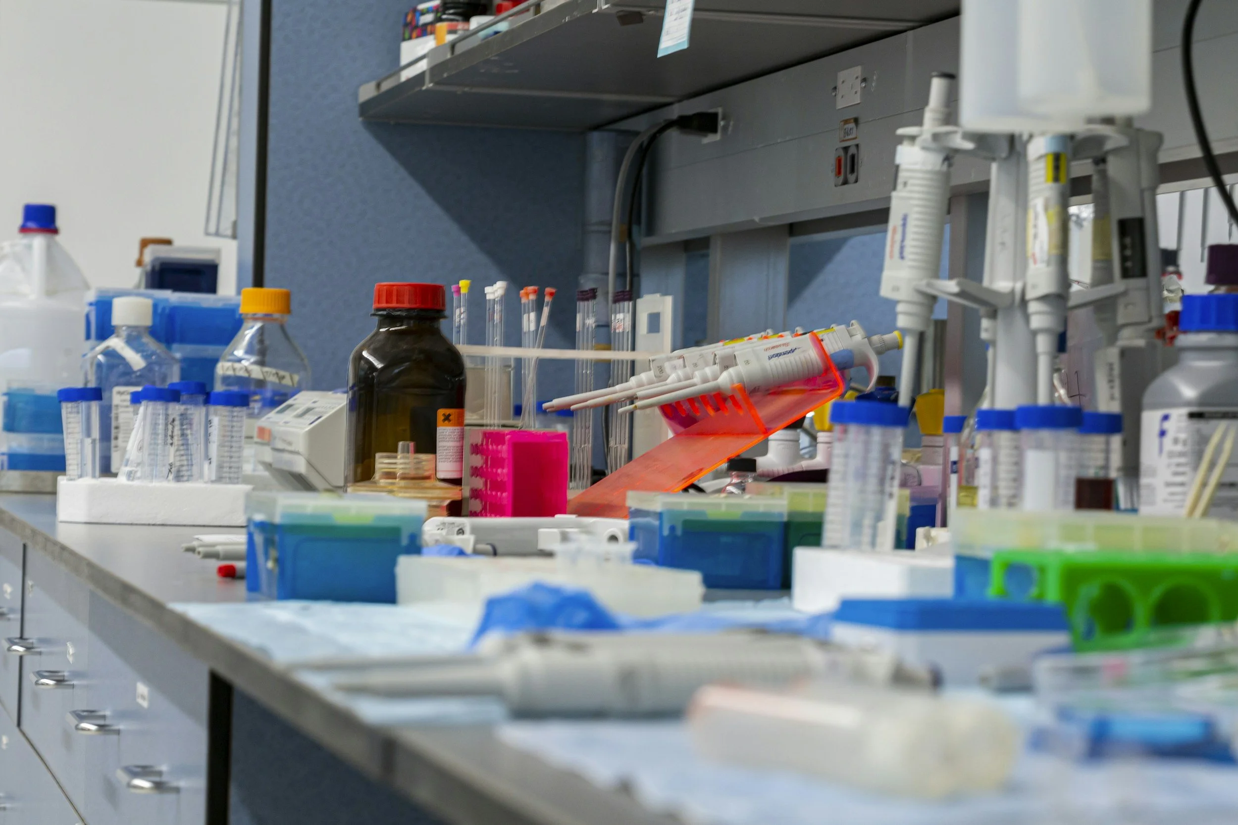 Laboratory work station with various bottles, test tubes, and medical supplies on a counter under a shelf