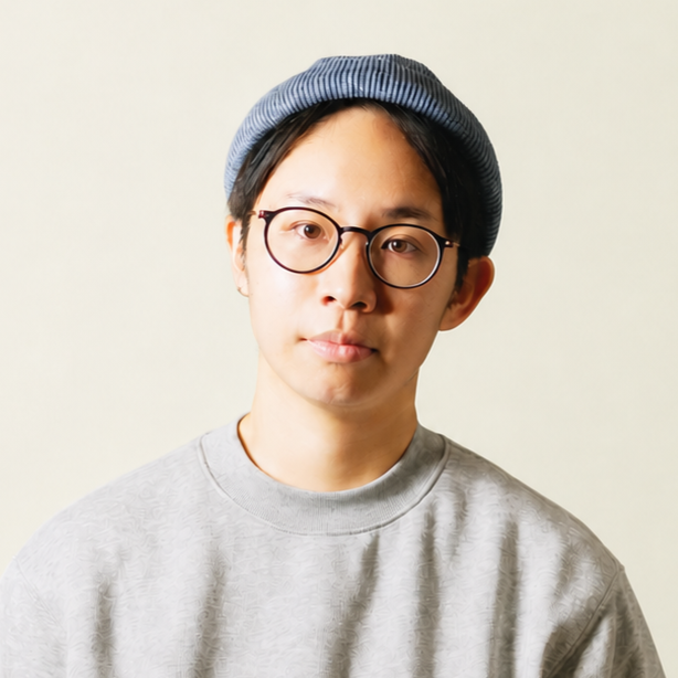 Young man wearing glasses, a blue striped beanie, and a light gray sweatshirt, standing against a plain light background.