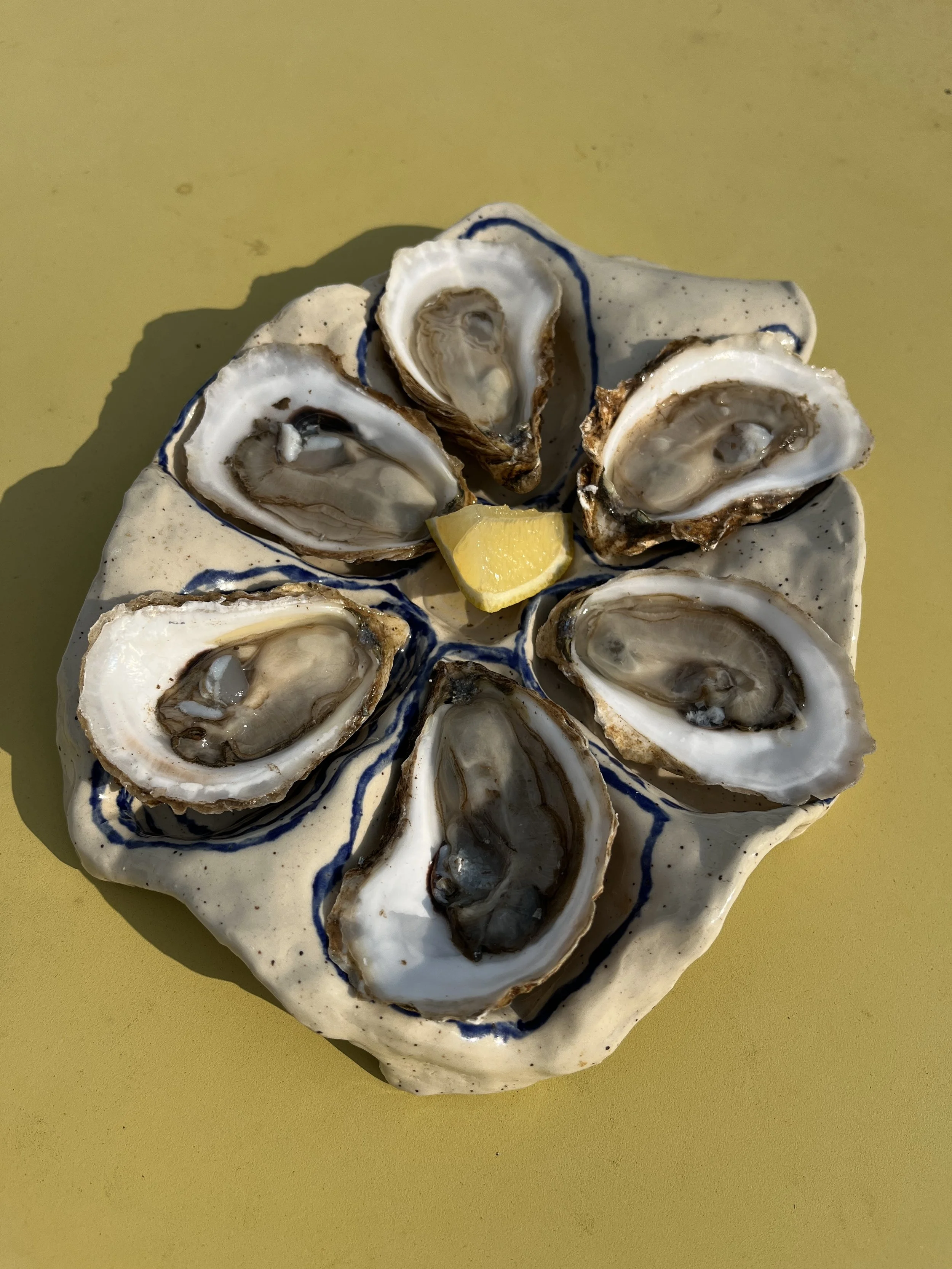 A ceramic plate holding open oyster shells with a lemon wedge in the center.
